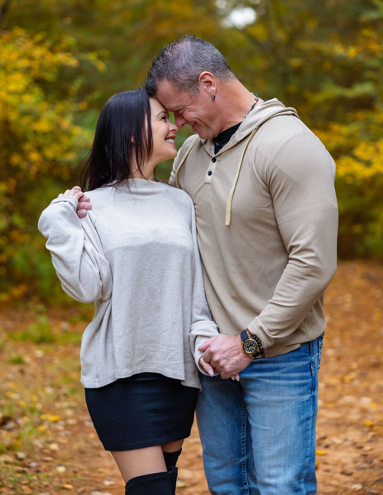 A couple shares an intimate moment on a path surrounded by autumn foliage in a park setting.