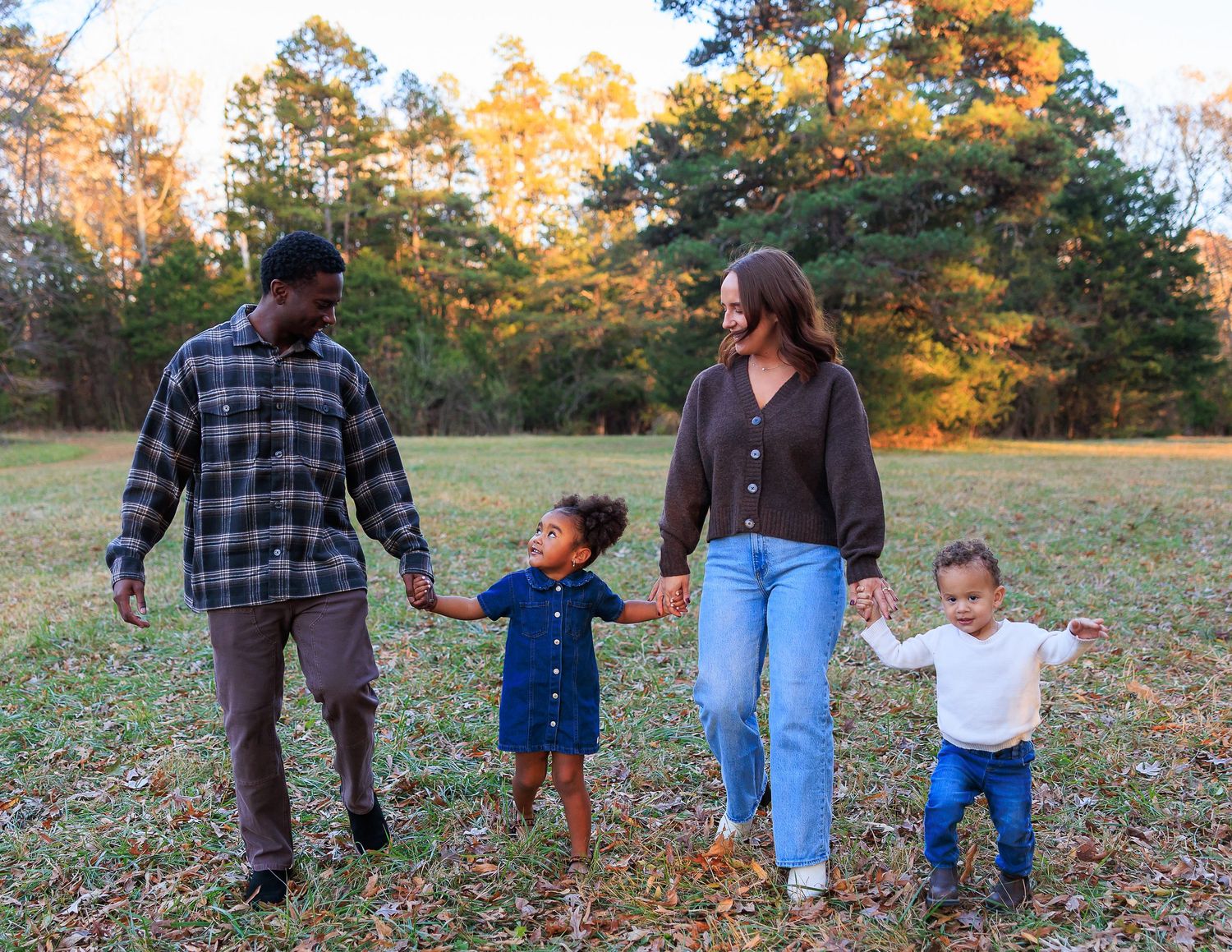A family walks hand in hand through autumn foliage during a fall photoshoot in a park.