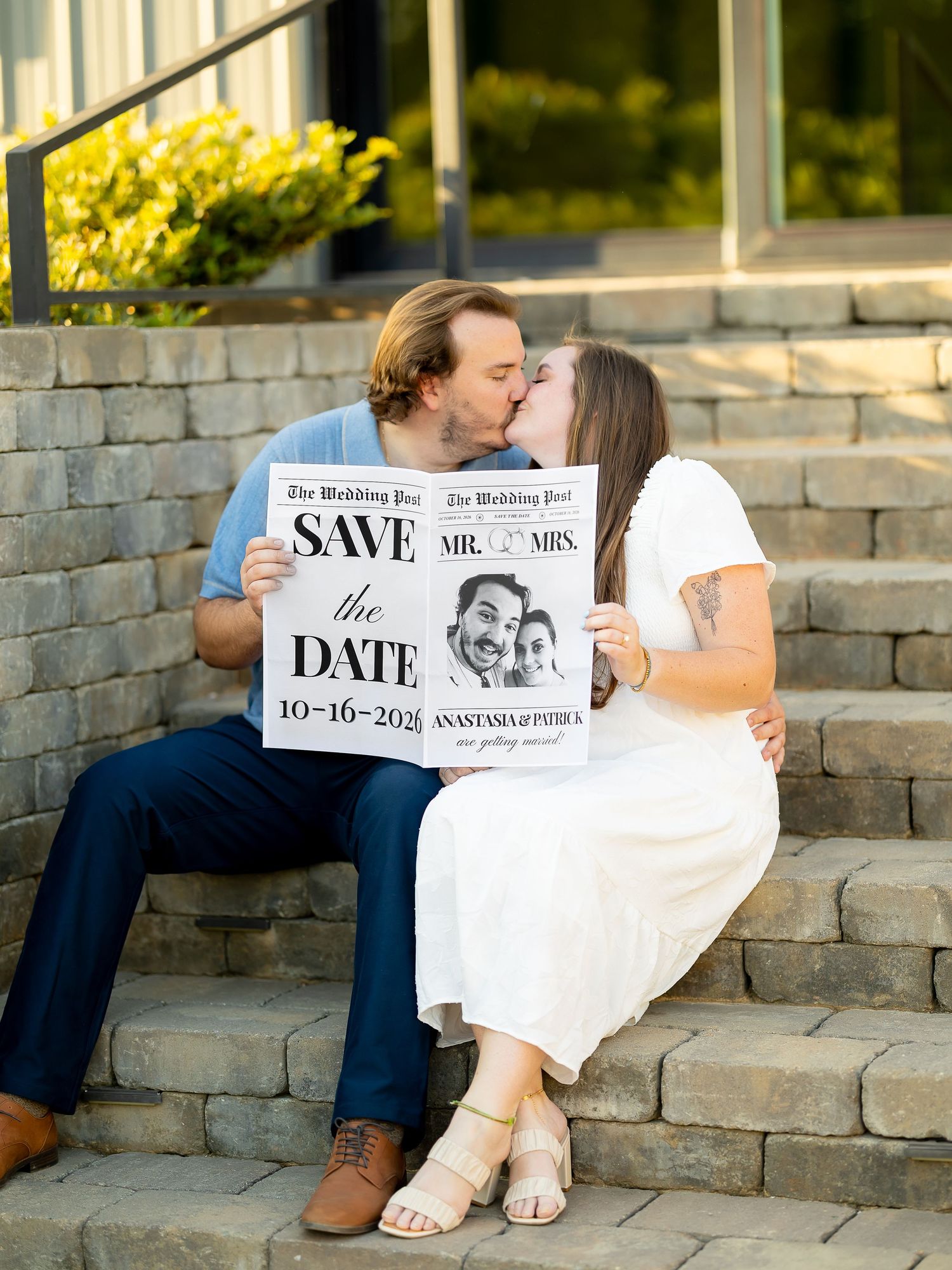 Couple kissing on stone steps holding a Save the Date newspaper sign for their October 16th wedding.