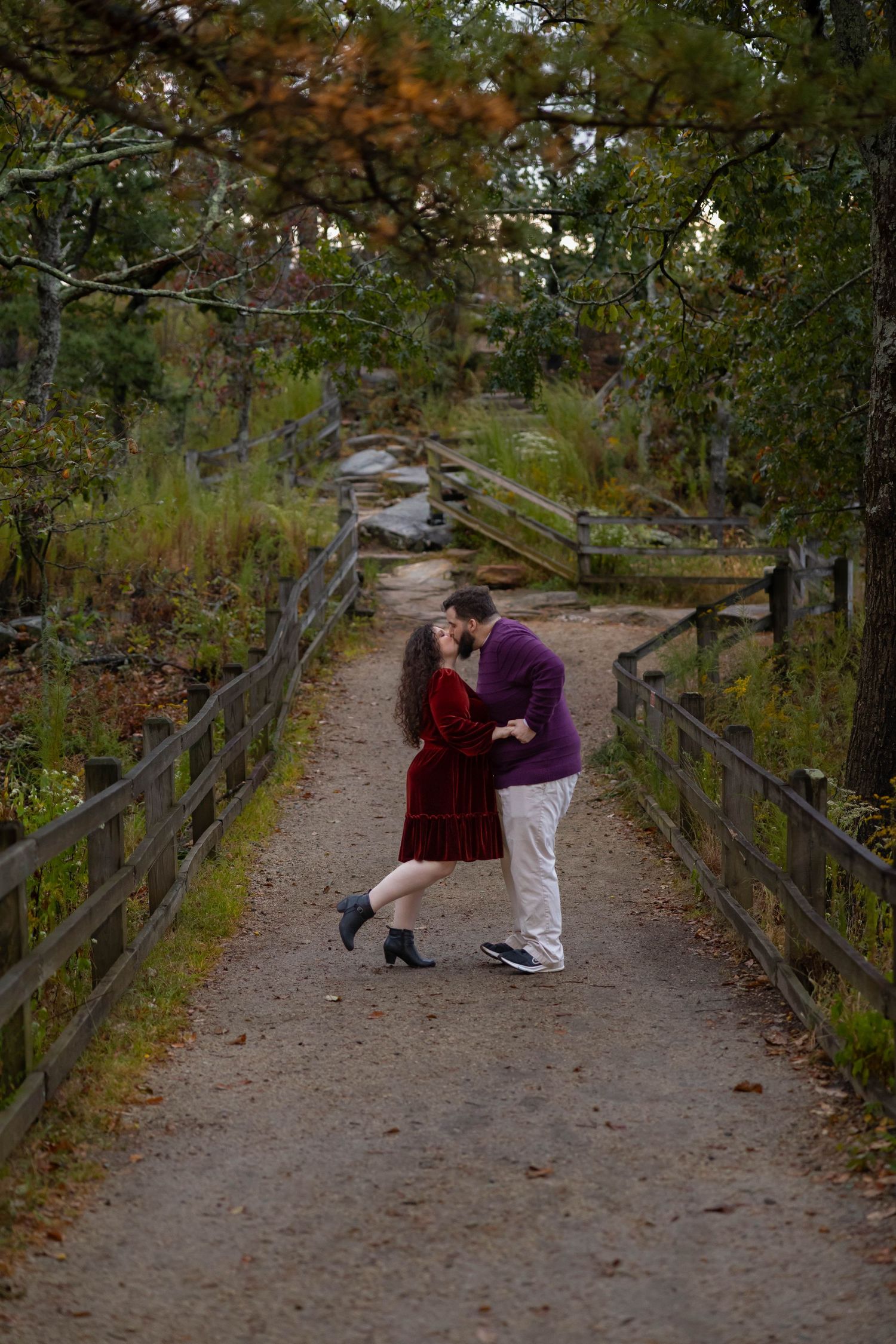 A couple shares a romantic moment on a wooden bridge surrounded by autumn foliage on a nature trail.
