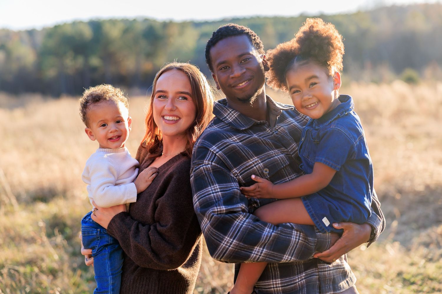 Happy family posing together outdoors in a sunlit field during golden hour.