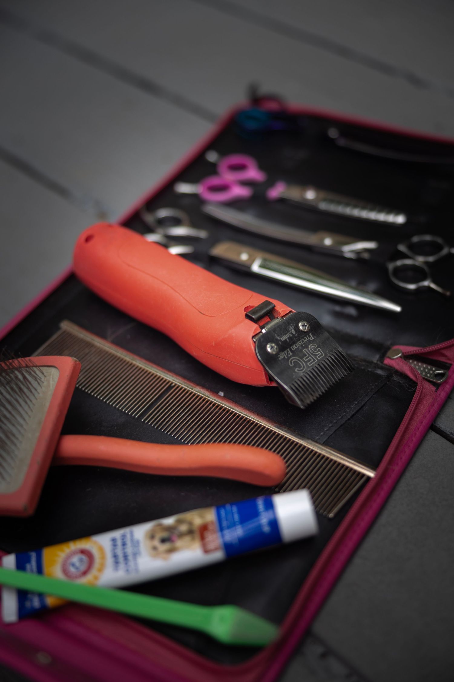 Professional pet grooming tools including clippers, combs, scissors and supplies arranged in a pink carrying case.