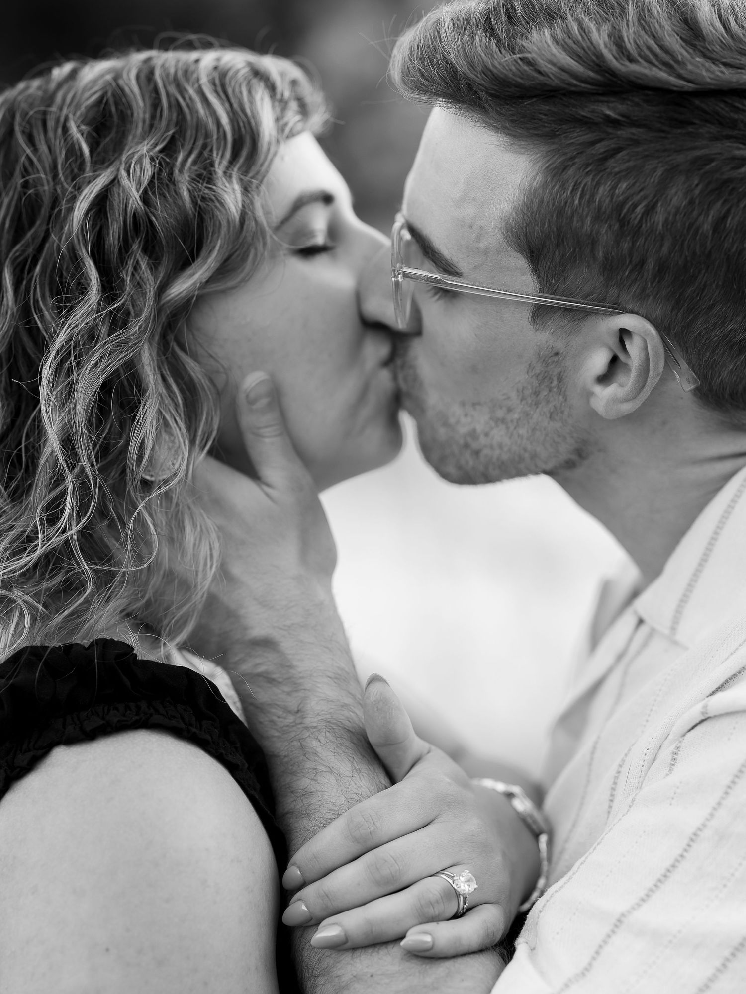Black and white photo of a couple sharing a romantic kiss, woman wearing an engagement ring.
