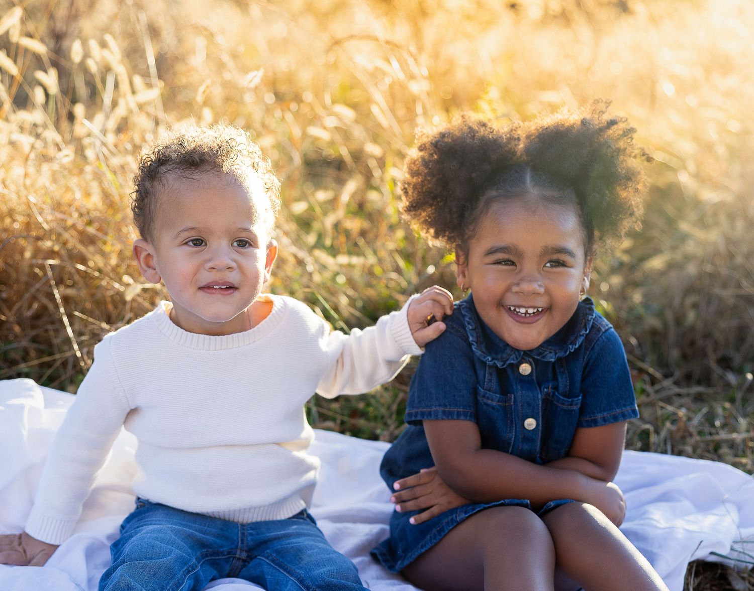 Two young children sitting together on a blanket outdoors during golden hour sunset.