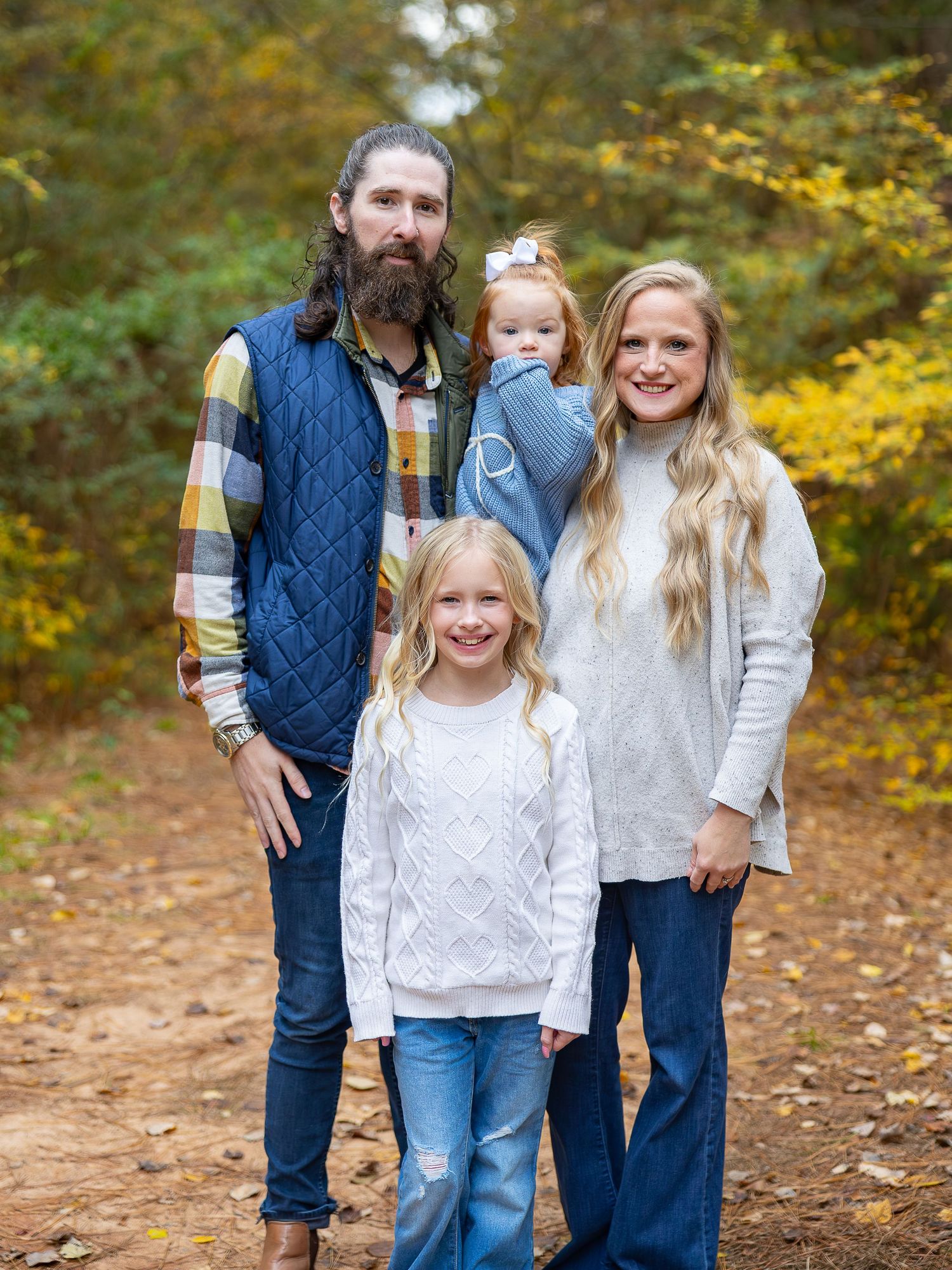 A family dressed in coordinating blue and white outfits poses together in an autumn forest setting.