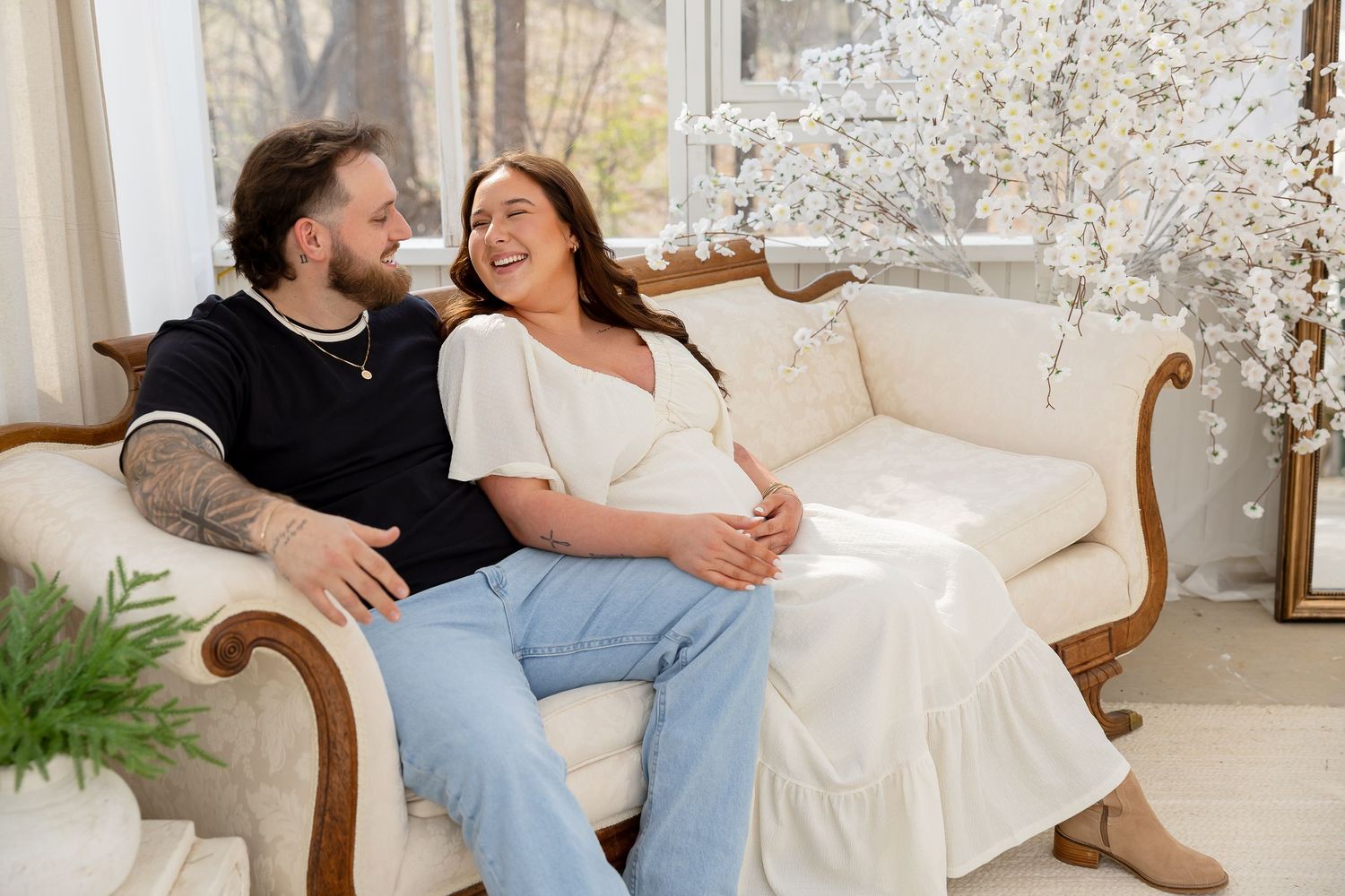 Couple sharing joyful moments together on an elegant white couch in a bright sunlit living room.