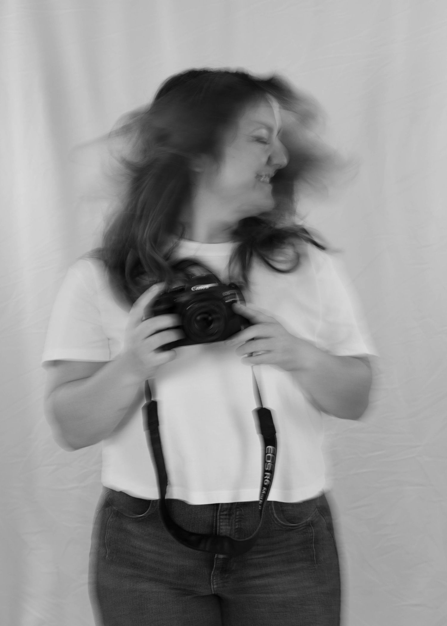 Motion blur photograph of someone in a white shirt holding a camera against a plain background.