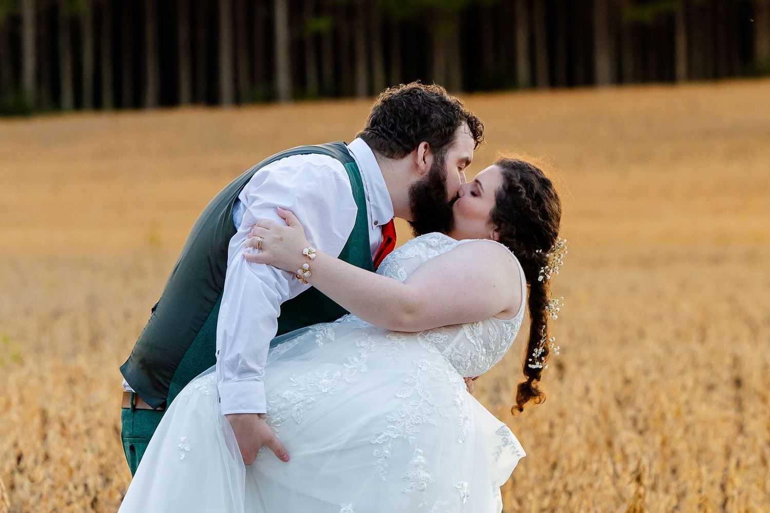Bride and groom share a romantic dip kiss in a golden wheat field during their outdoor wedding photo session.