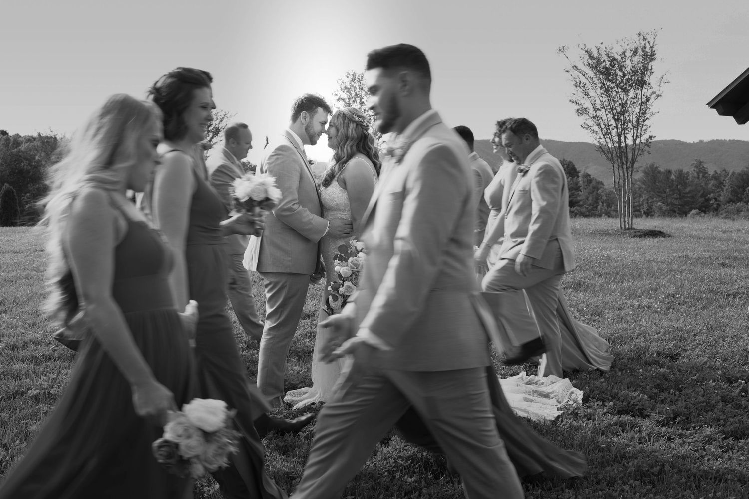 Black and white photo of wedding guests mingling and laughing together outdoors during a celebration.