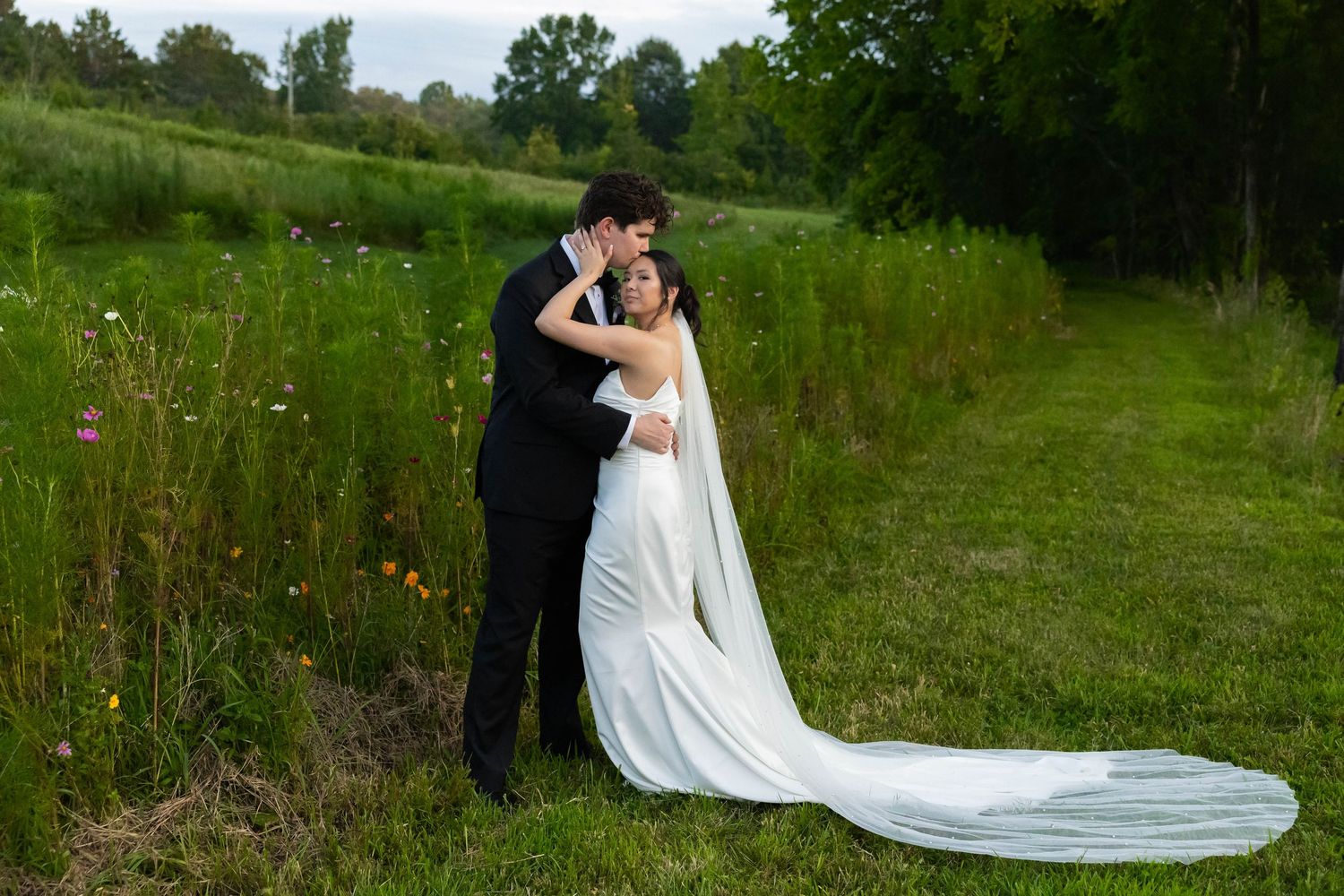 Wedding couple embracing in a scenic meadow with flowing white dress and green natural landscape.