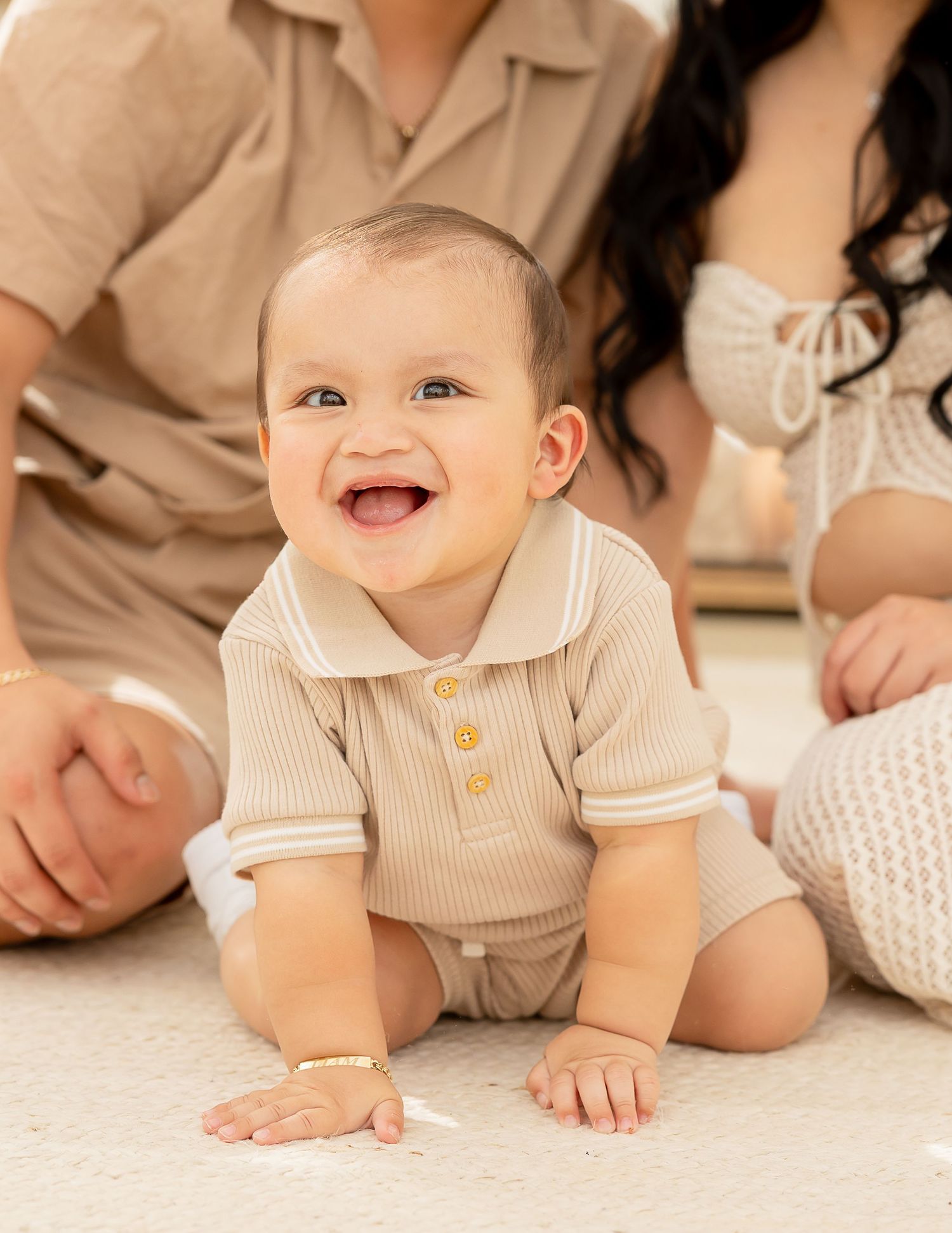 Baby in beige outfit crawls and smiles while playing on a light colored floor.