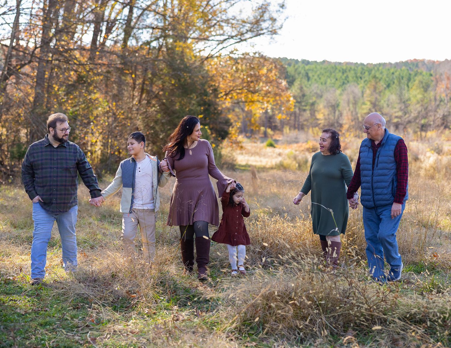 Group of people walking together through a scenic autumn field with golden grass and trees in the background.