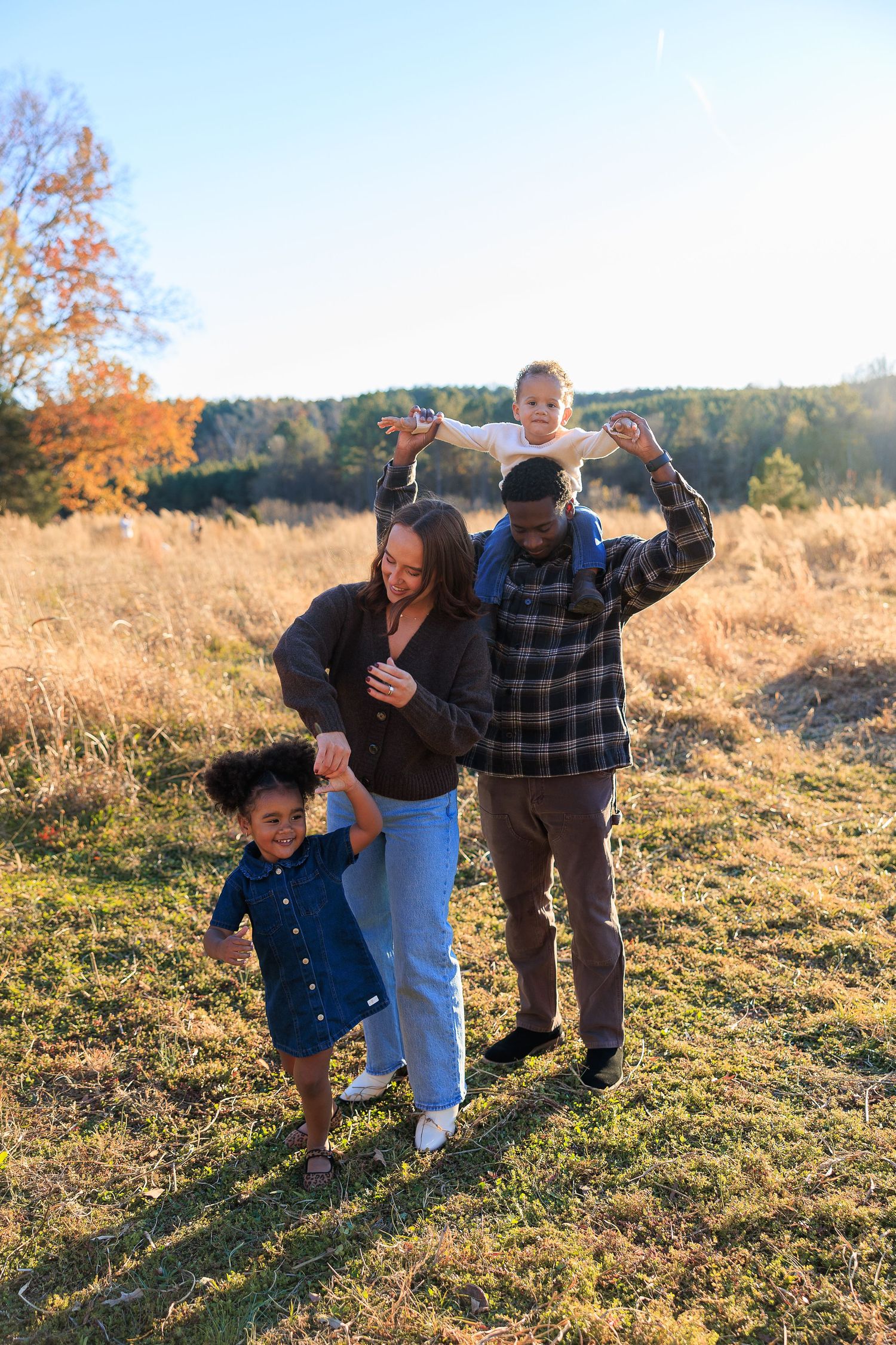 Family plays and laughs together in a sunny autumn field during golden hour.