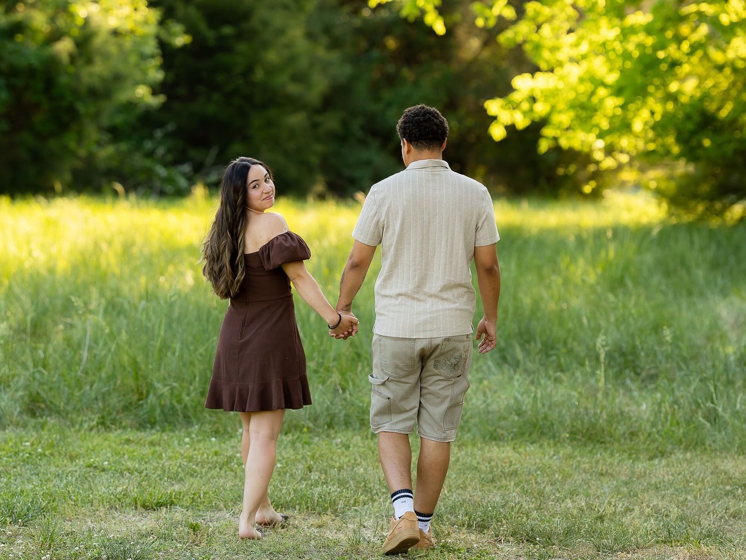 Young couple holding hands walking through a lush green park on a sunny day.