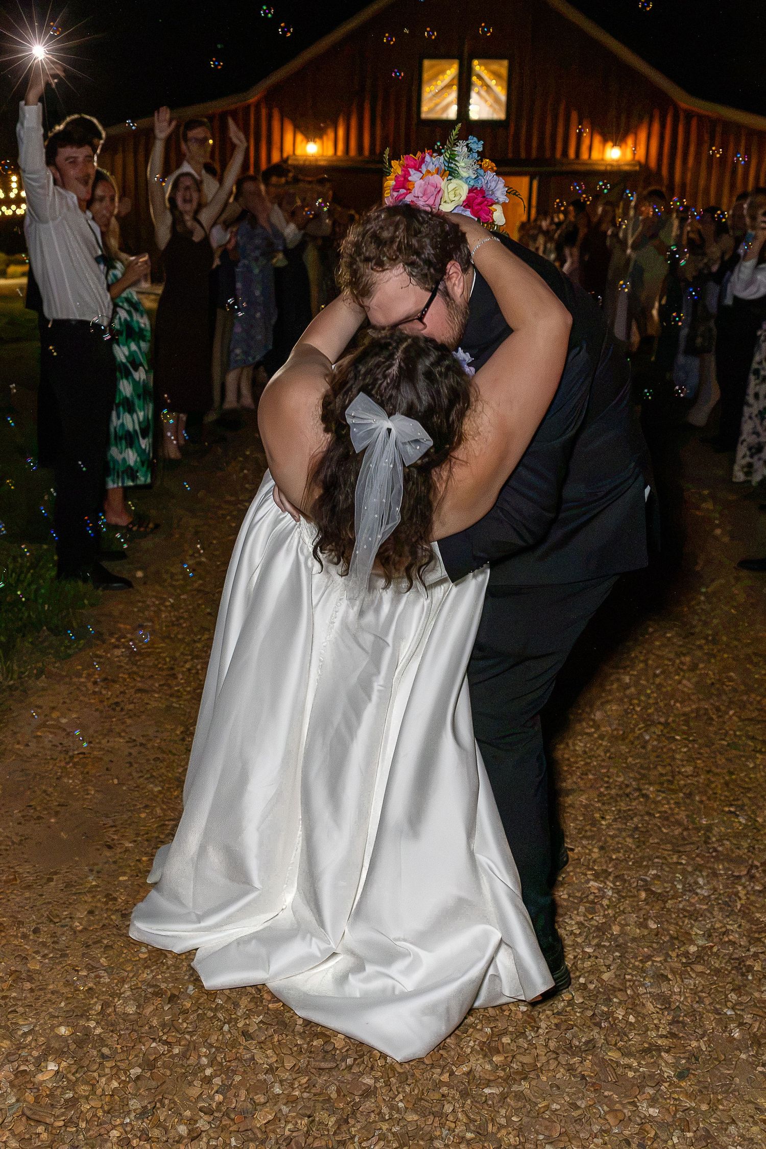Bride and groom share a romantic dip kiss at night outside a barn wedding reception.