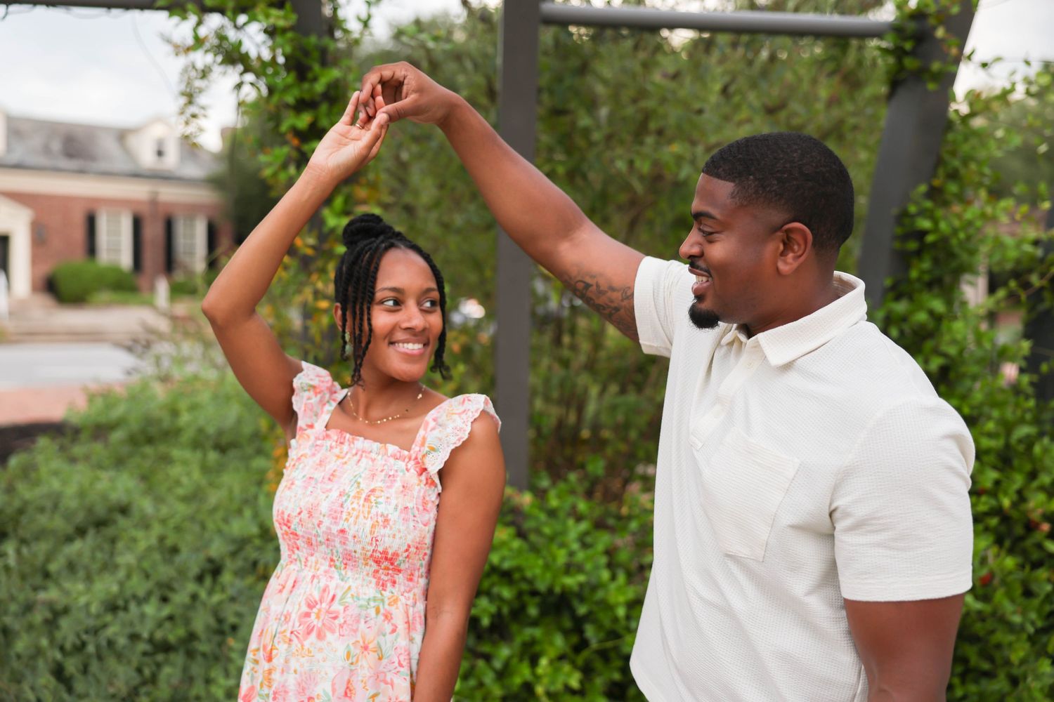 A tender romantic engagement photo session in a lush garden setting with elegant pink and white outfits.