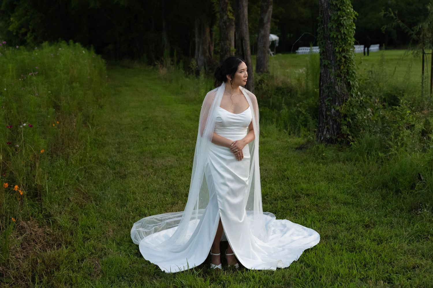 A bride in a flowing white wedding dress twirls gracefully in a lush green outdoor setting.