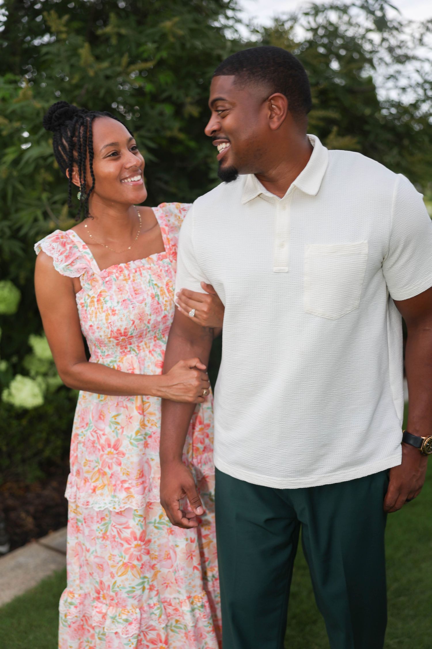 A couple laughing together outdoors in coordinating white and floral outfits during a warm day.