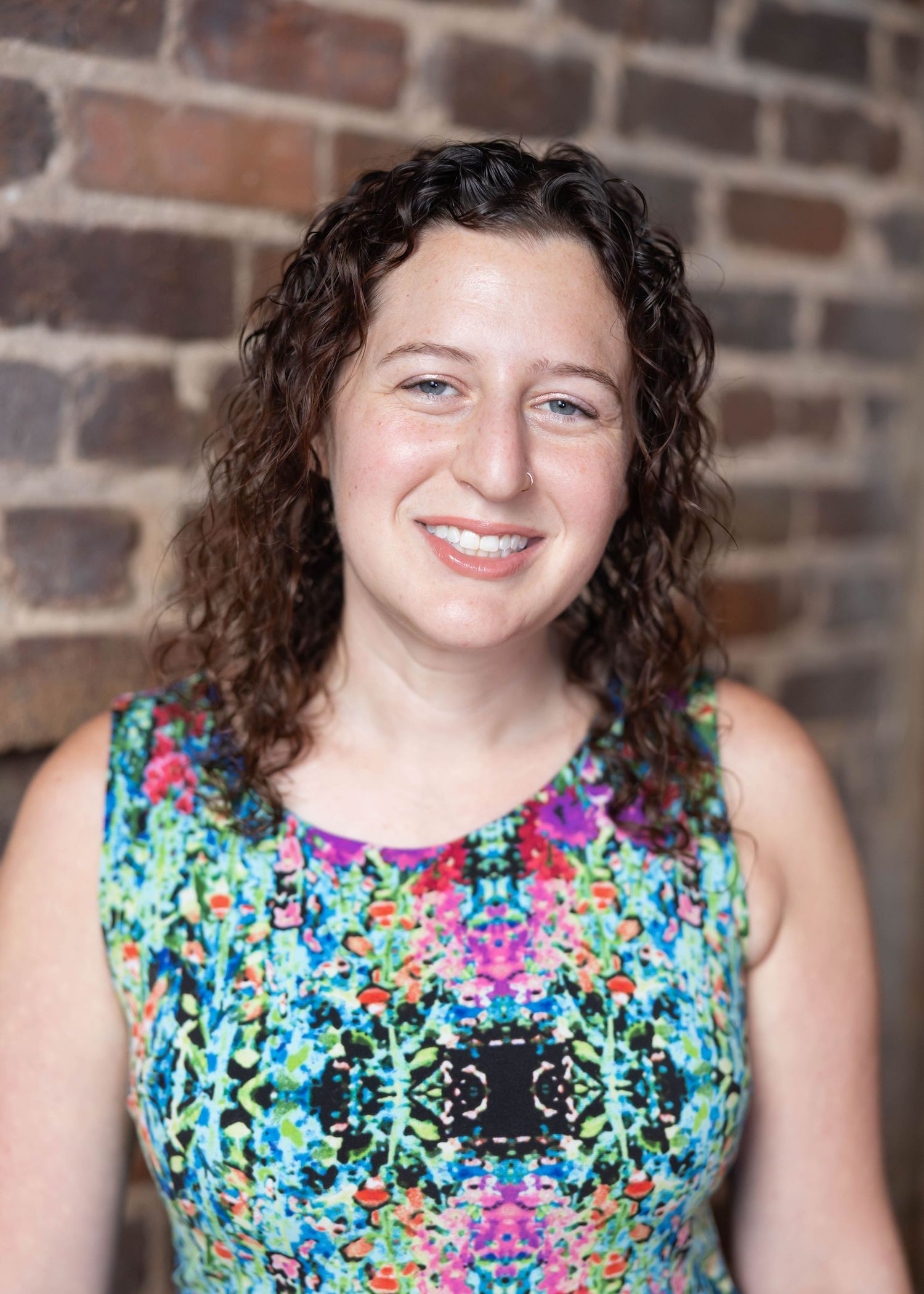 Person in sleeveless floral dress smiling against brick wall in a sequence of four similar portrait shots.