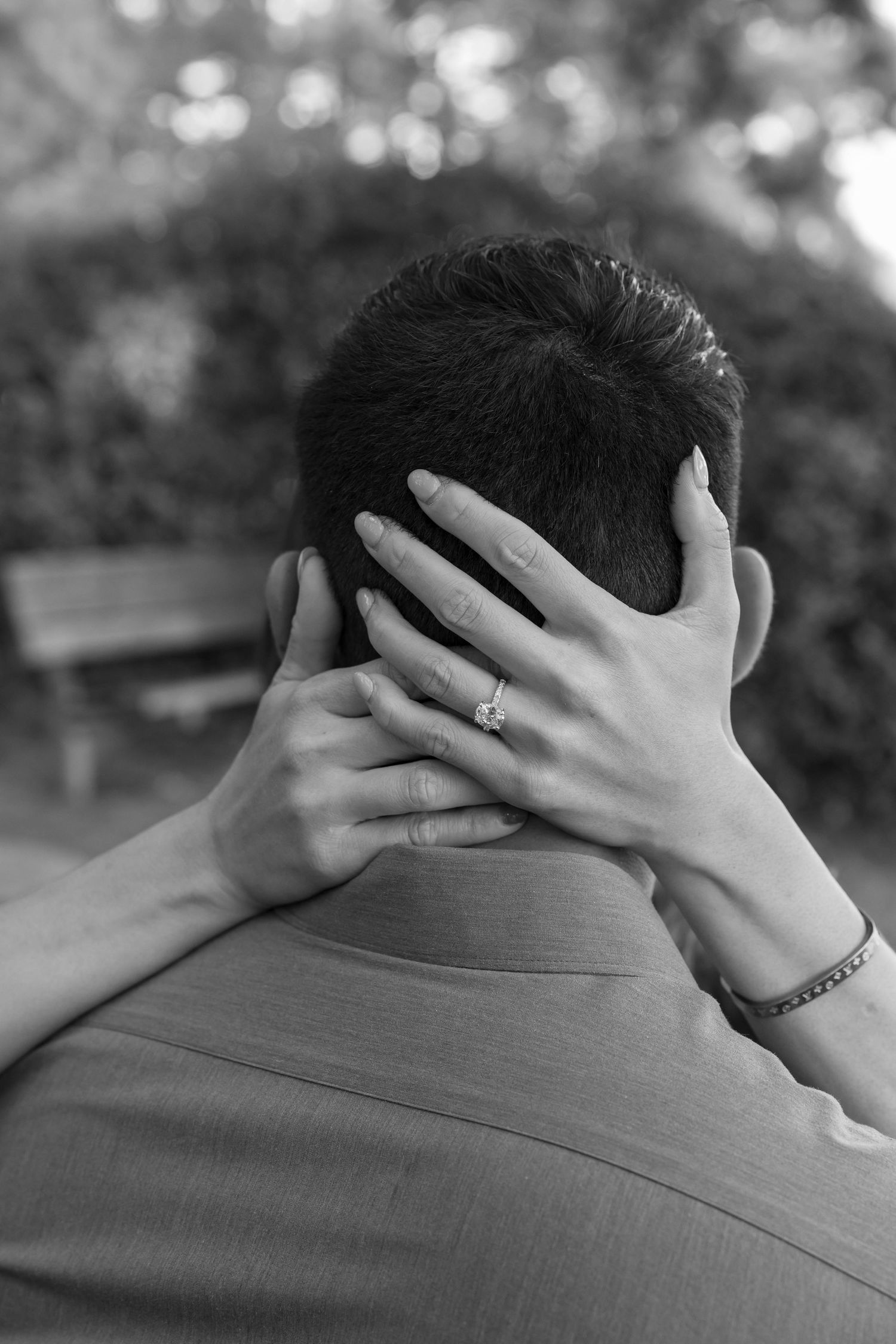 A black and white photo showing hands with a ring and bracelet clasped behind a head from behind.