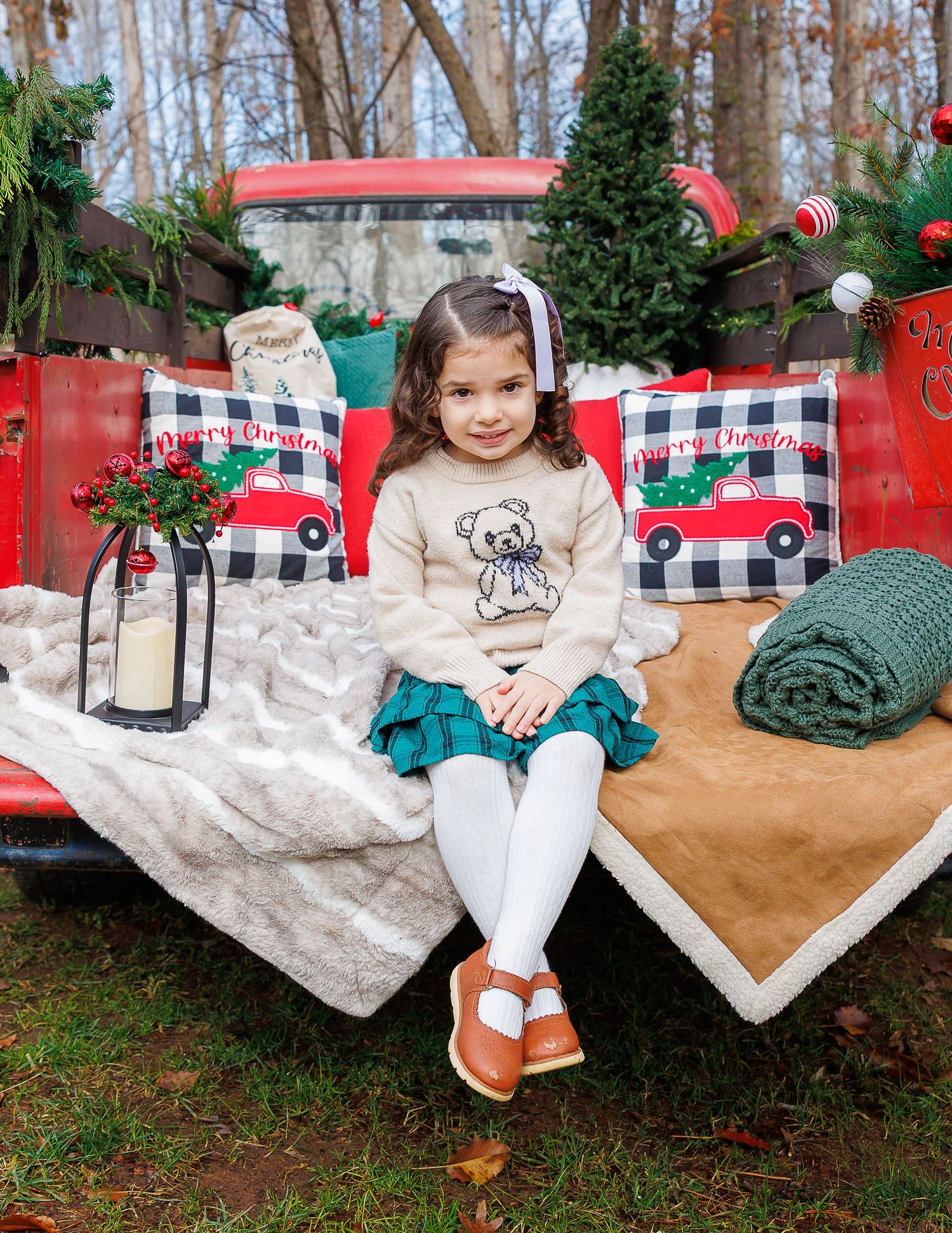 A festive holiday photo session setup with buffalo plaid blankets and Christmas decorations in an outdoor woodland setting.