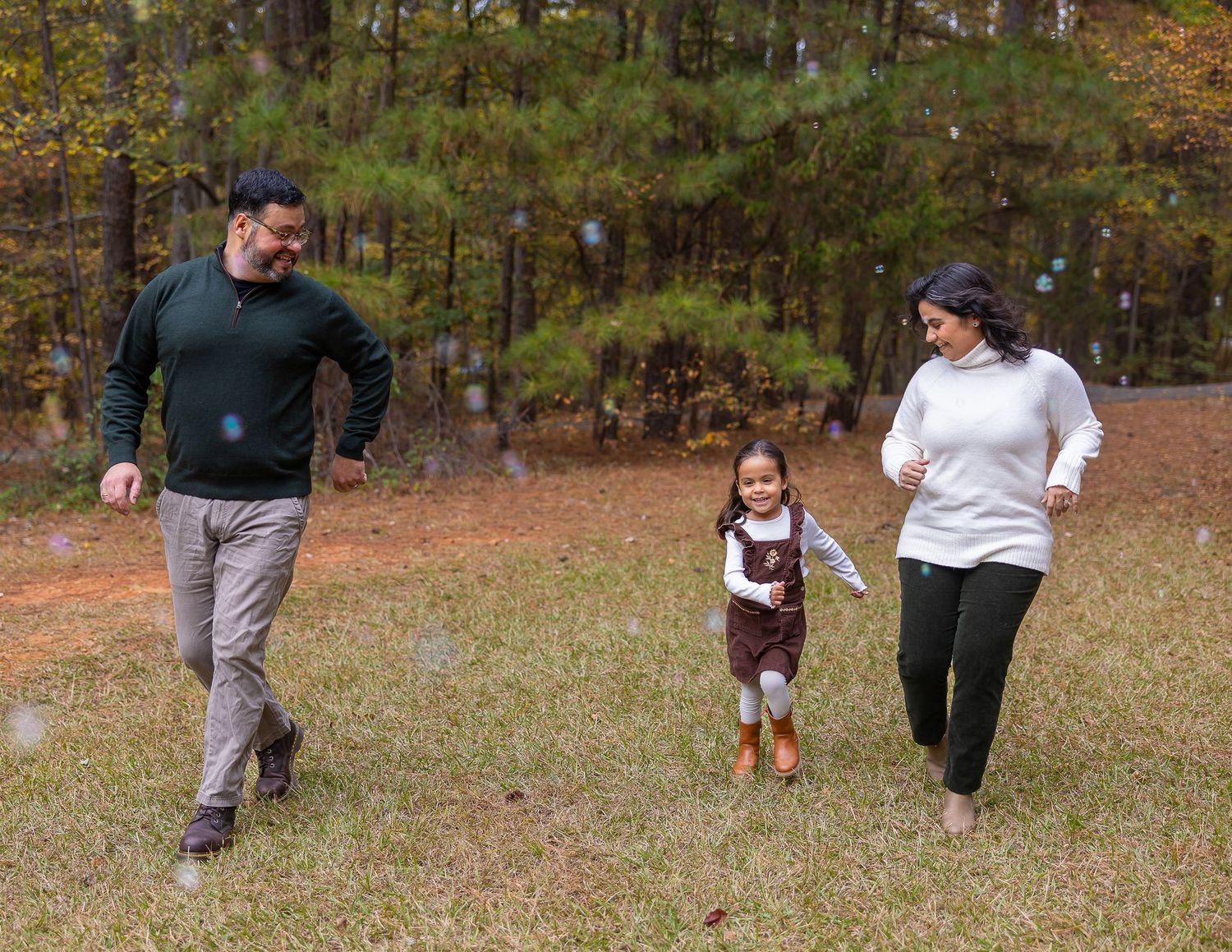 Three people running and playing together on autumn grass with trees in the background.