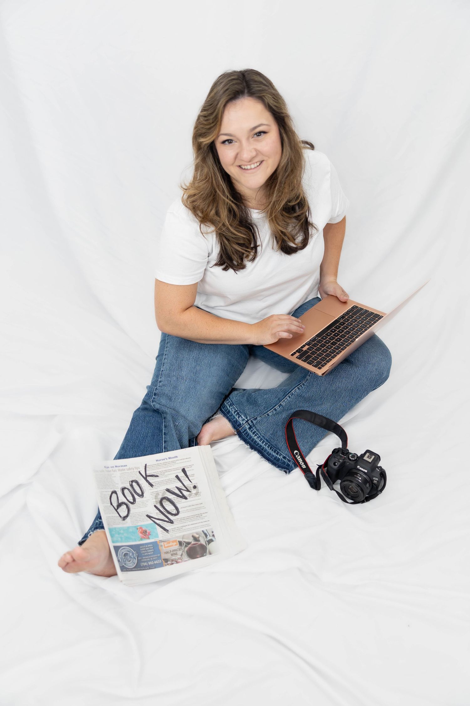 Content creator seated on white fabric with laptop, headphones and written materials for recording a podcast episode.