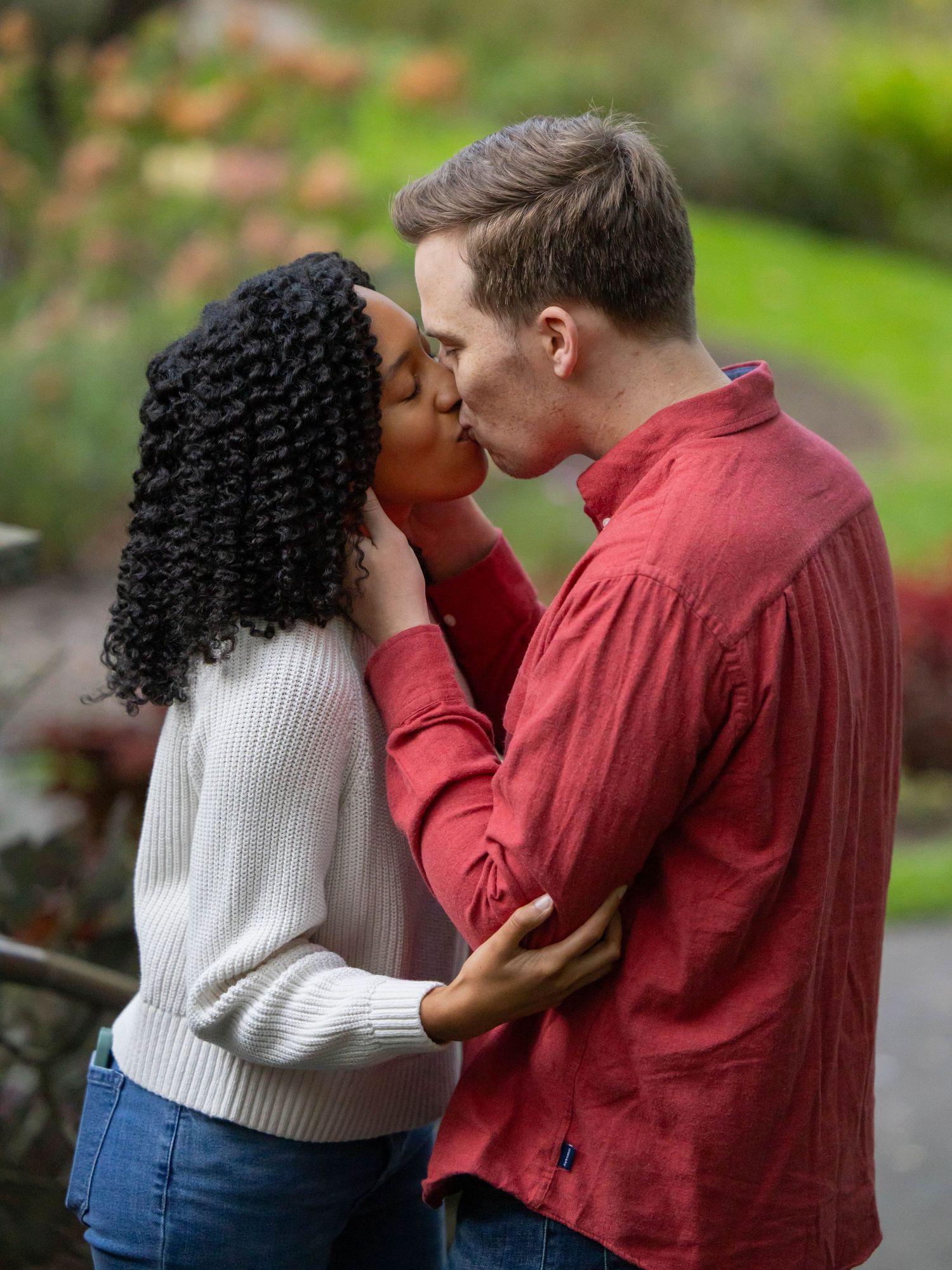 Romantic couple embracing in a garden setting wearing red and white sweaters.