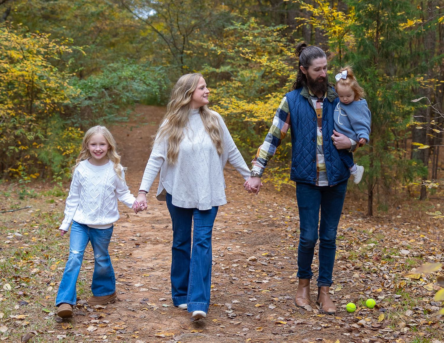 Family walking together through autumn woods wearing matching denim and casual attire on a fall day.
