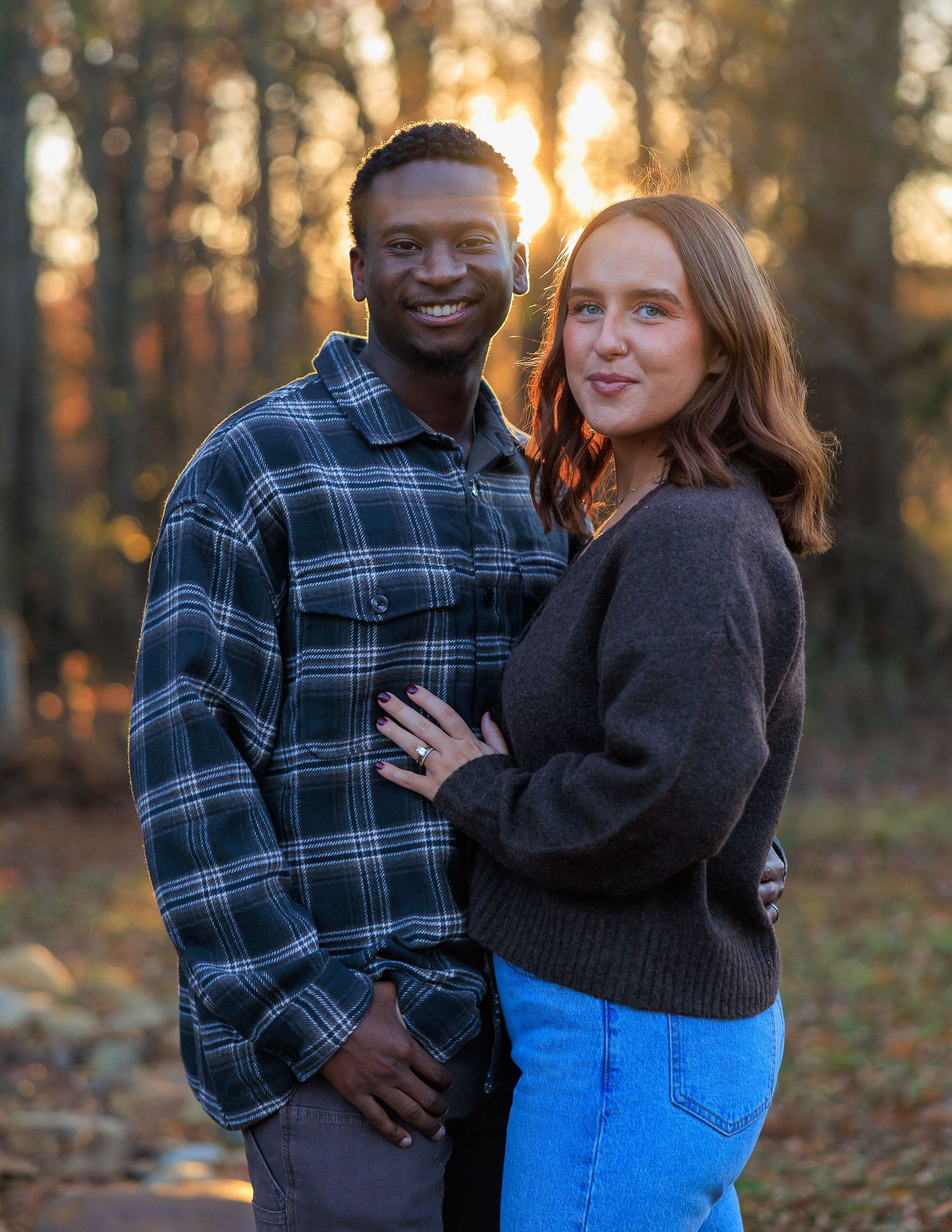 Couple embracing outdoors during golden hour sunset in autumn forest setting with fallen leaves.