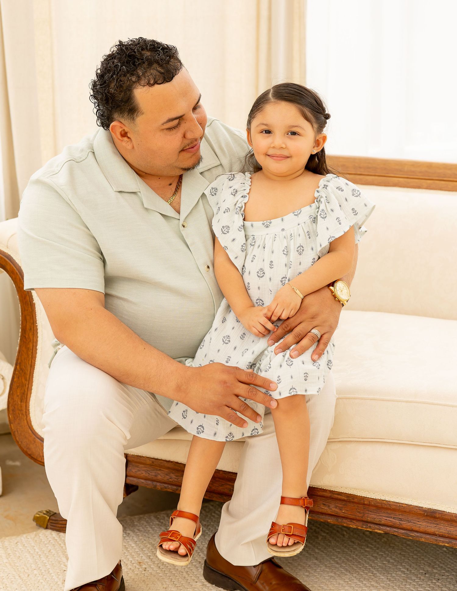 Intimate family portrait session showing tender moments on a white sofa in a sunlit room.