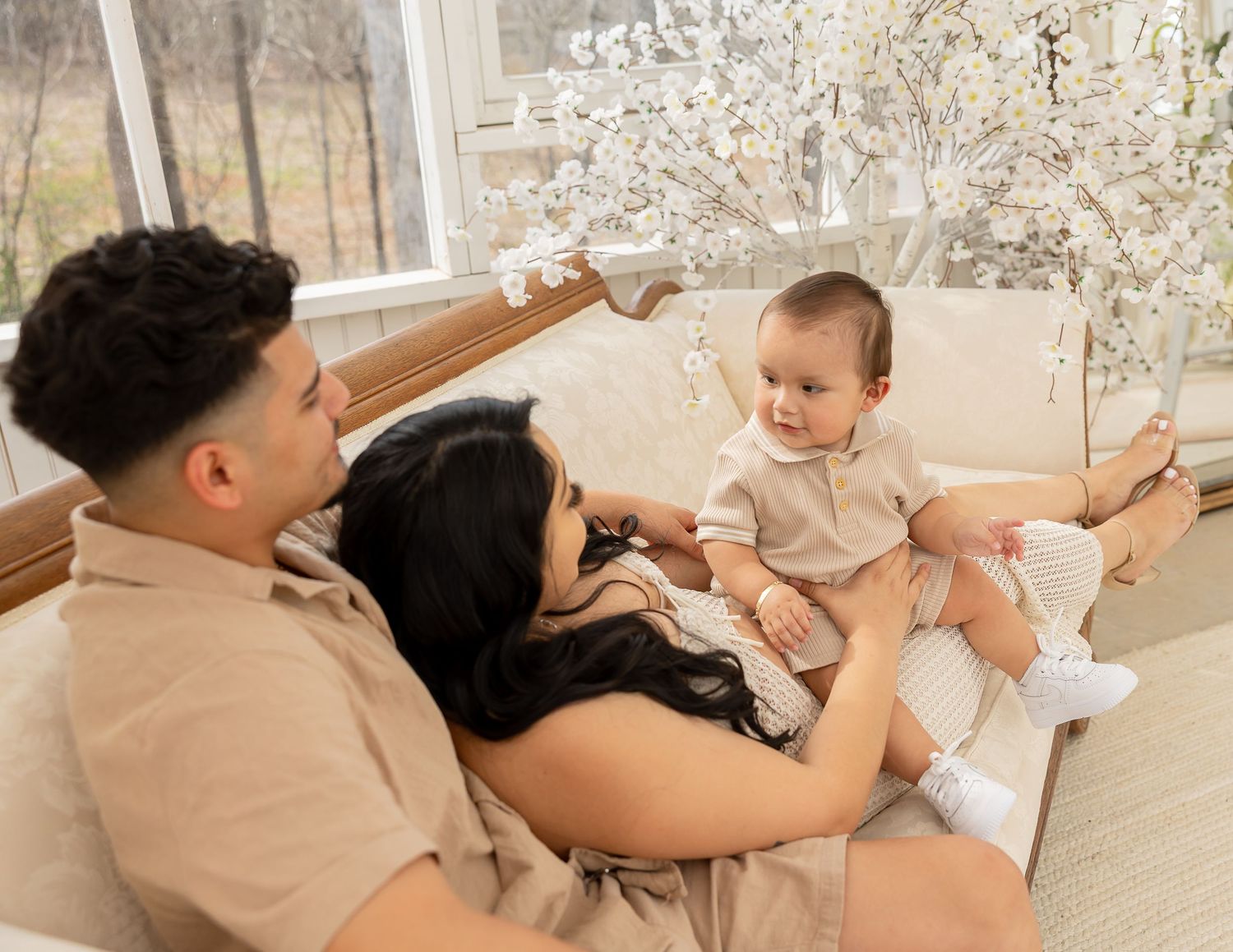 A family relaxes together on a couch near blooming cherry blossoms visible through a window.