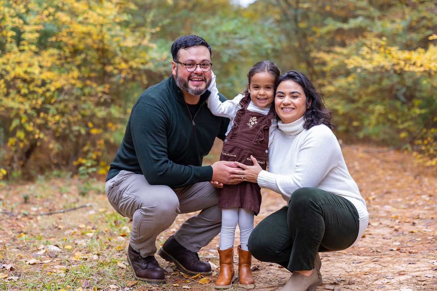 A playful family moment captured outdoors in autumn with a brown dog on a leaf-covered forest path.