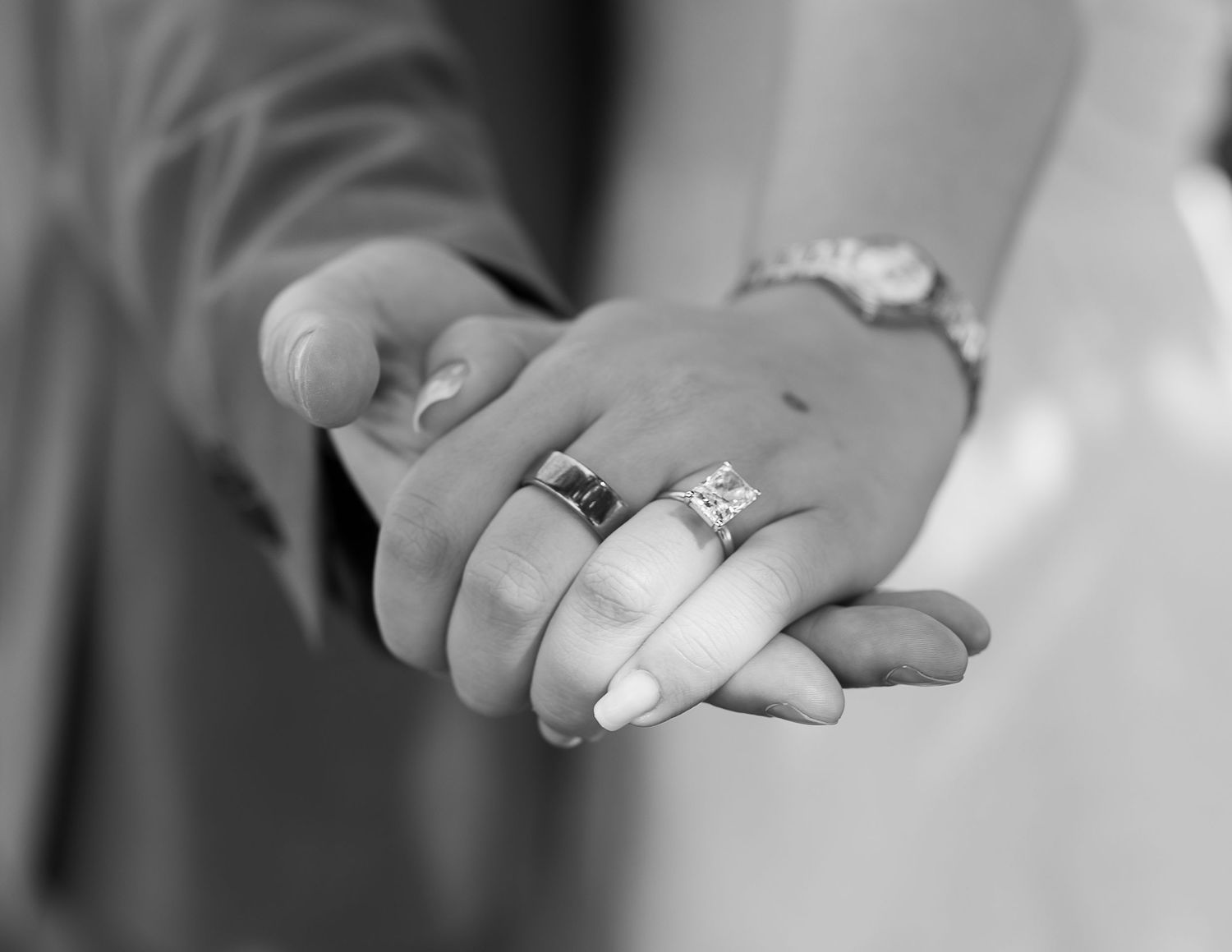 Close-up black and white photo of hands with engagement rings showing wedding jewelry details.