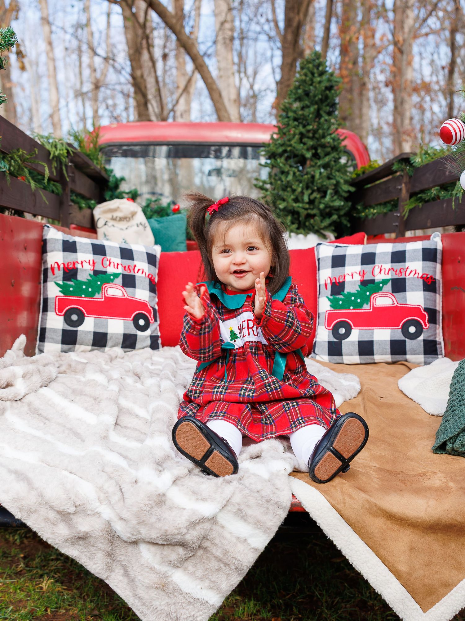 Festive holiday scene with plaid pillows, Christmas decor, and snow-like blankets against a vintage red truck backdrop.