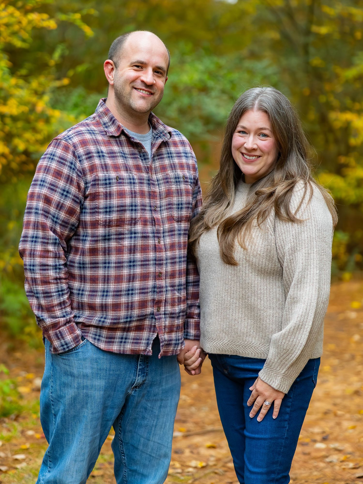 A couple wearing plaid and sweaters share loving moments in an autumn forest setting with golden foliage.