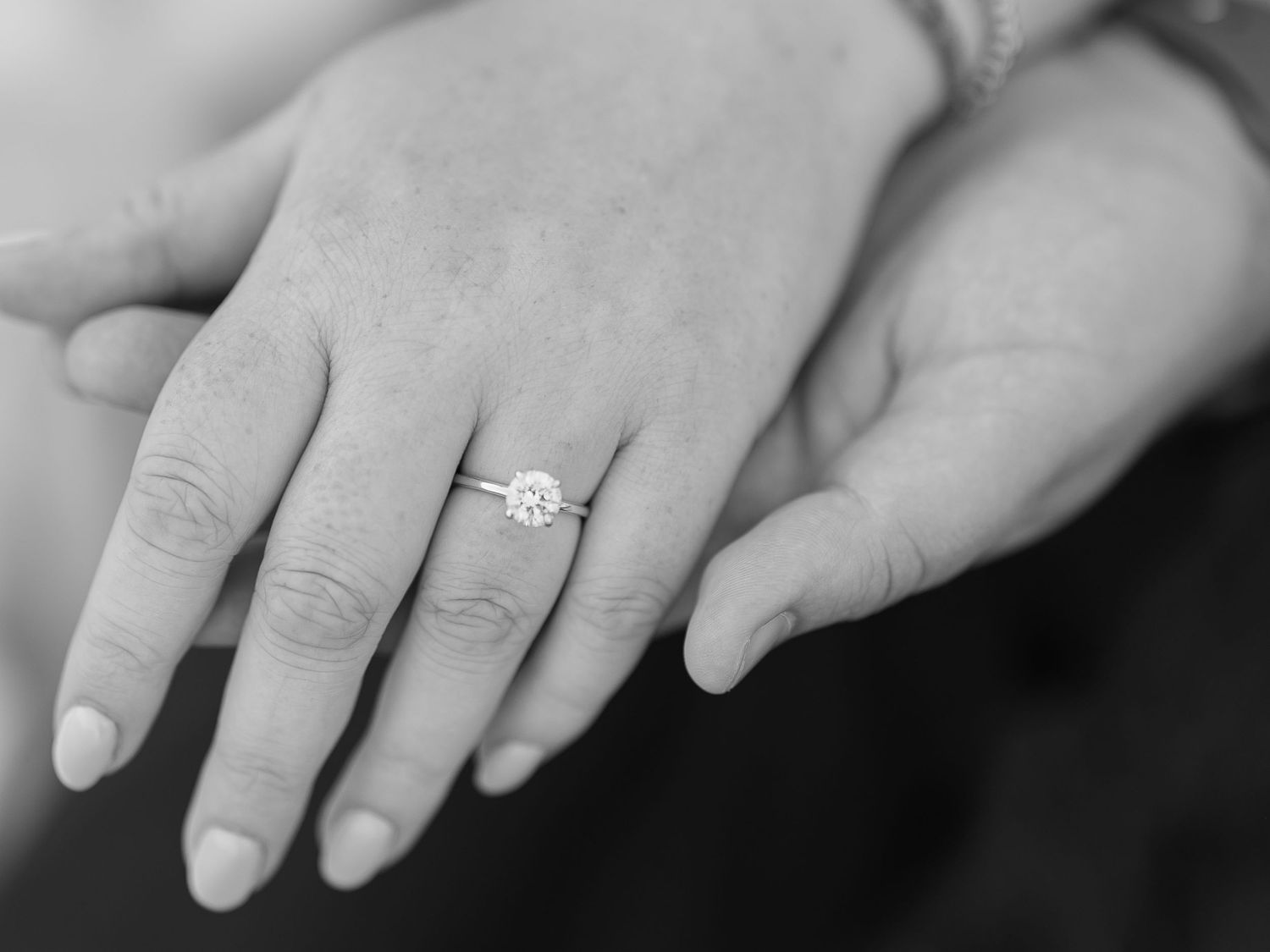 Black and white close-up of hands displaying a solitaire diamond engagement ring.