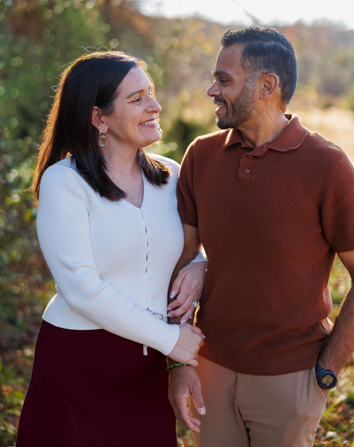 A couple laughs and embraces while enjoying a romantic autumn photoshoot outdoors in warm sweaters.