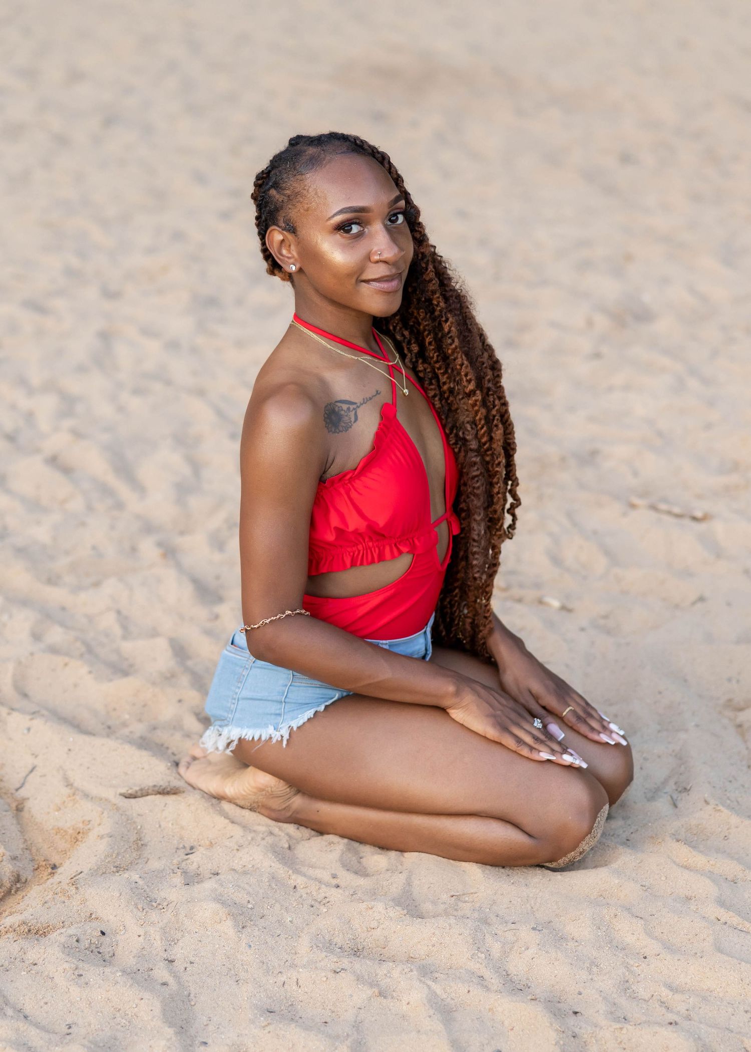 Person in red swimsuit relaxing on sandy beach with long braided hair flowing back.