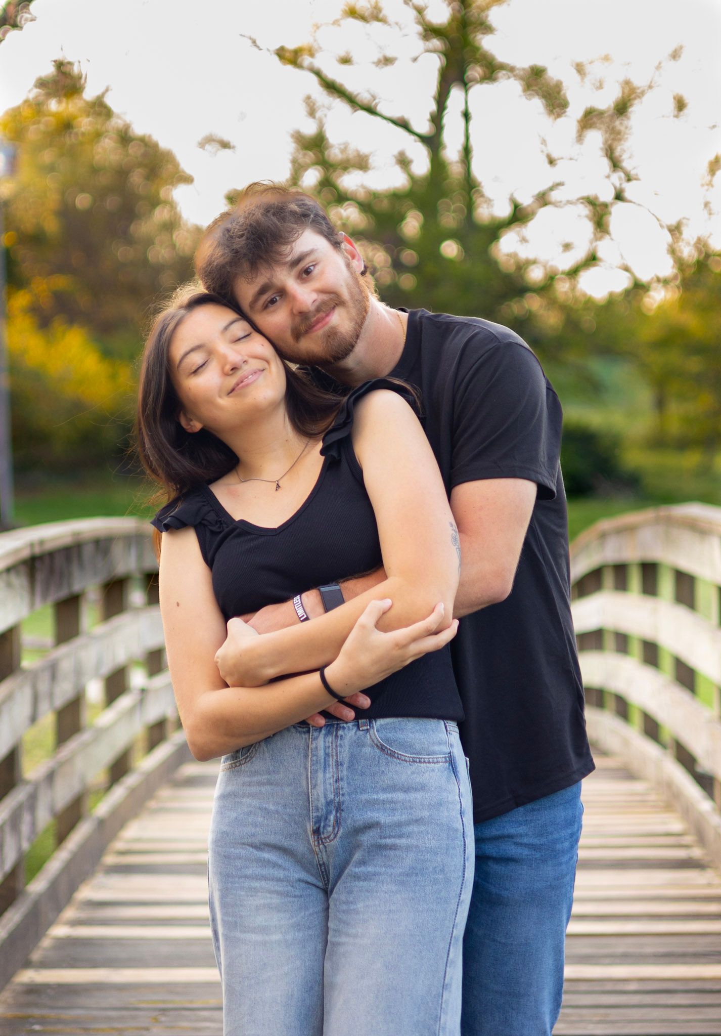 A couple shares a tender moment together while standing on a wooden bridge in a park during golden hour.