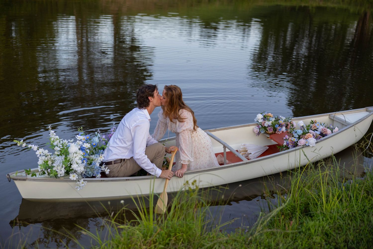 A romantic couple sits in a white canoe on a tranquil lake surrounded by lush greenery.