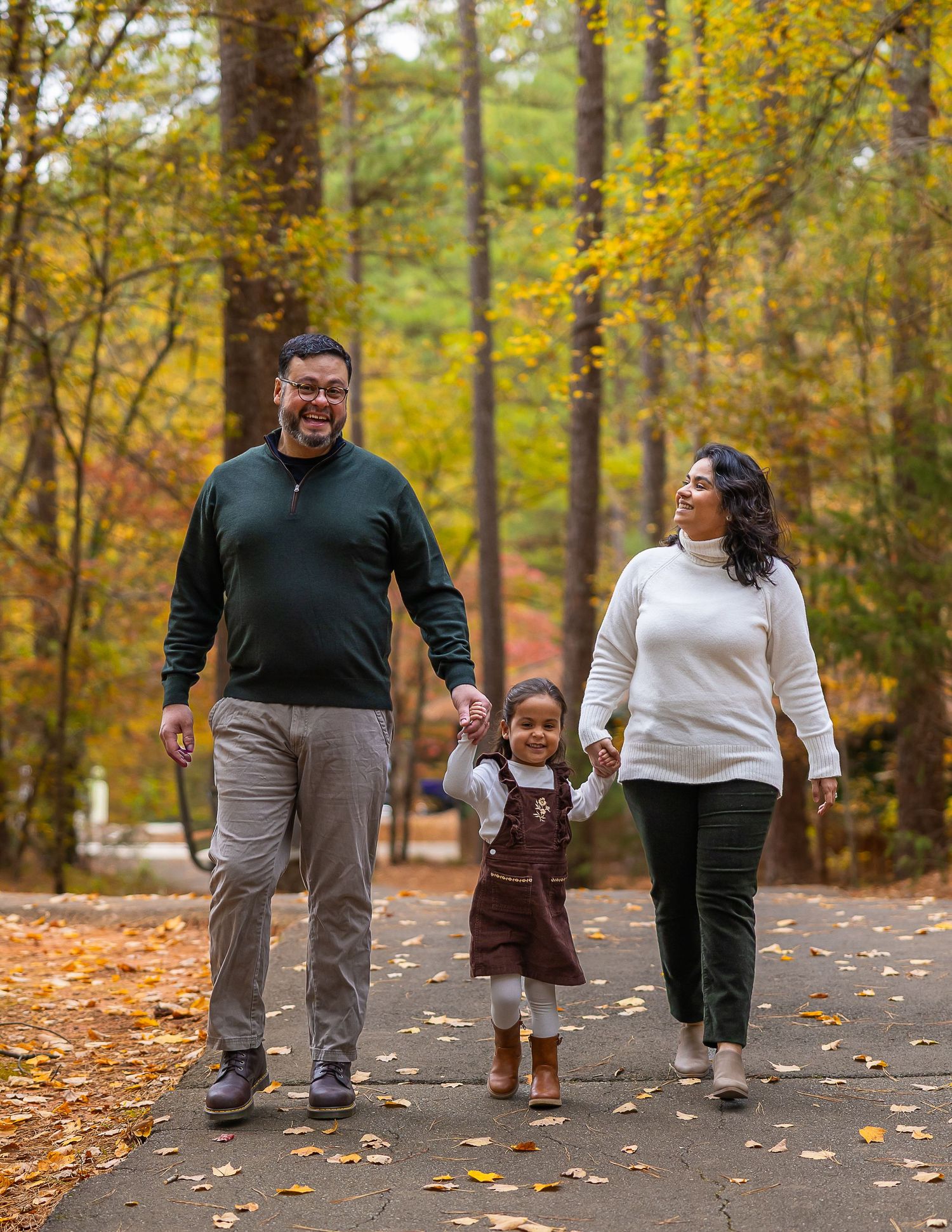 A family takes an autumn stroll together on a leaf-covered path surrounded by golden foliage in the woods.