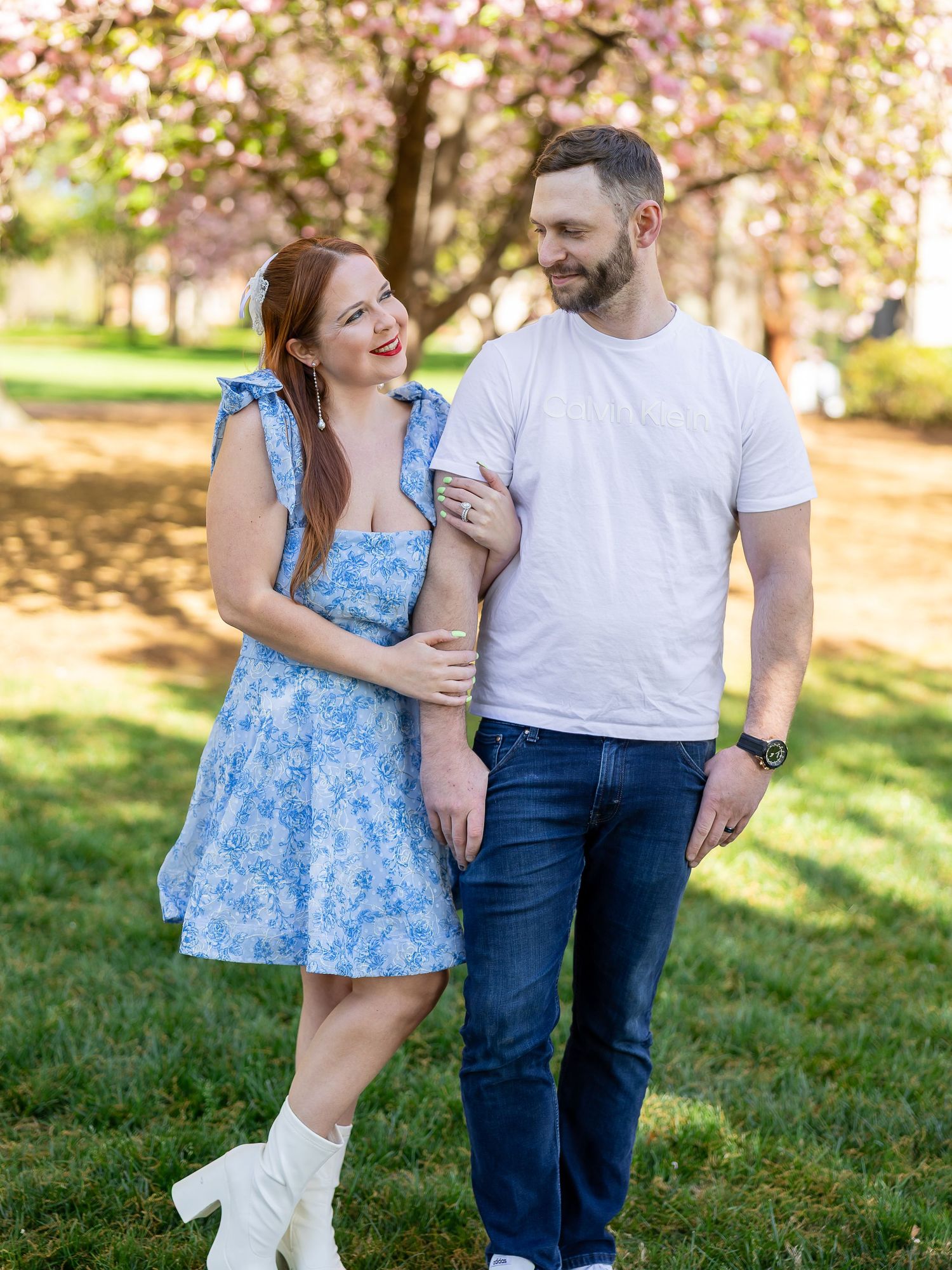 A smiling couple embracing in a park with blooming trees in the background.