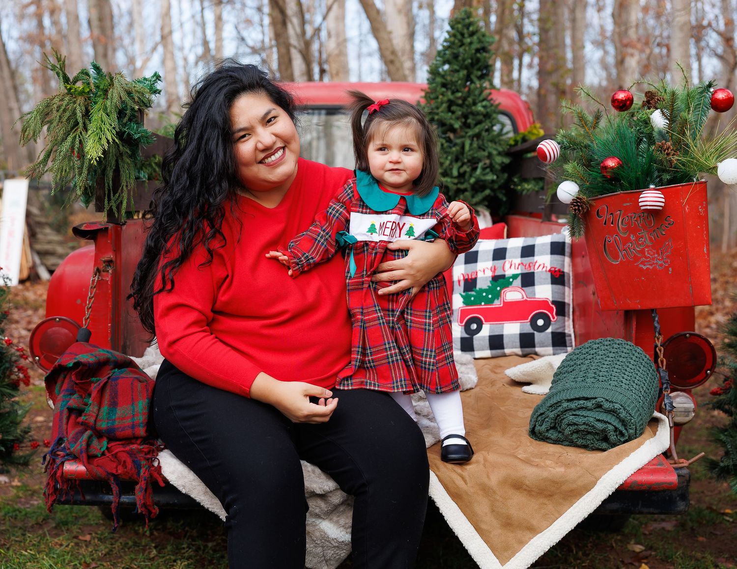 A festive holiday photo session featuring a red vintage truck decorated with Christmas ornaments and greenery.
