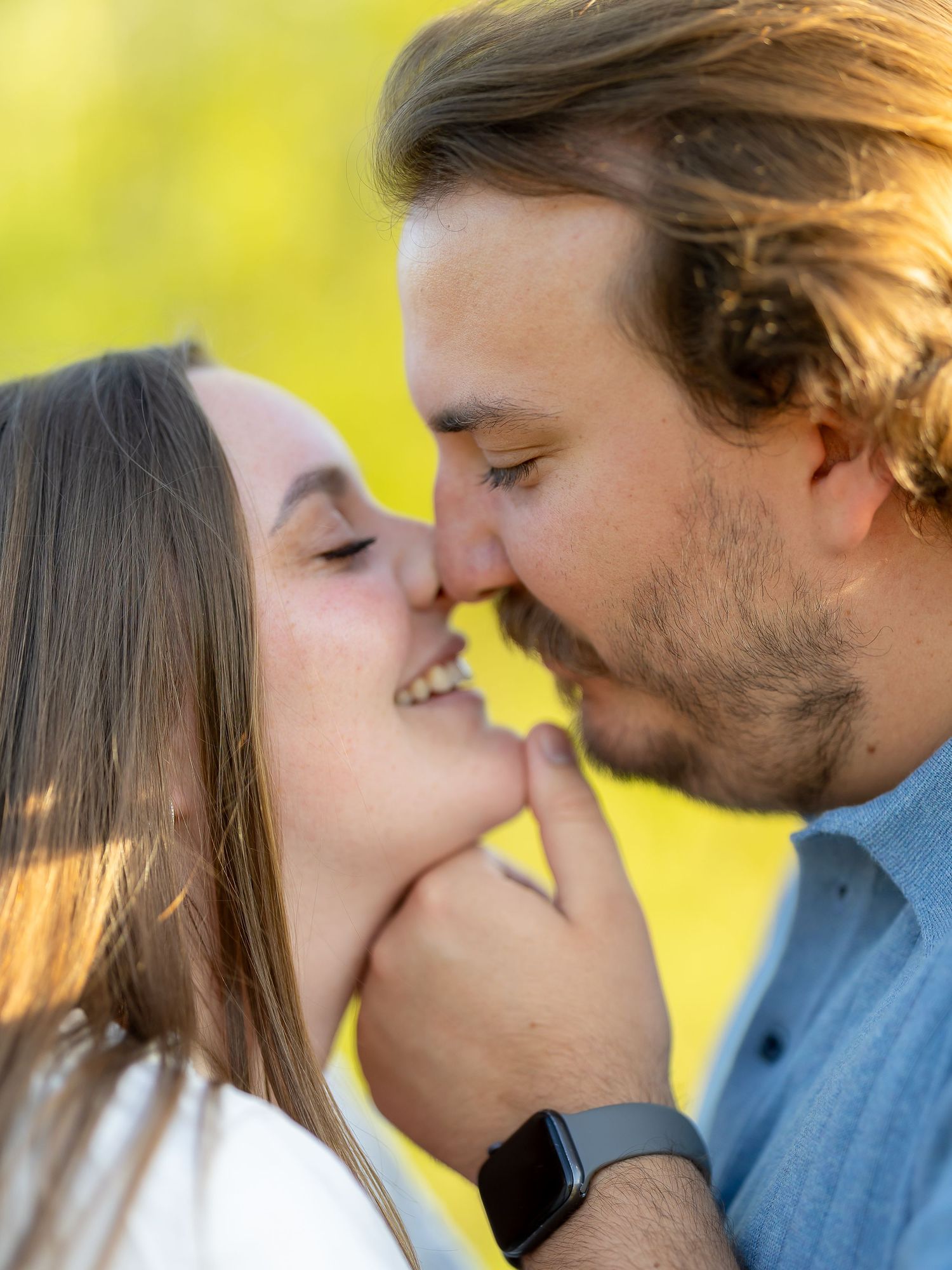 A couple shares a tender romantic moment, nearly kissing outdoors with warm golden bokeh background.