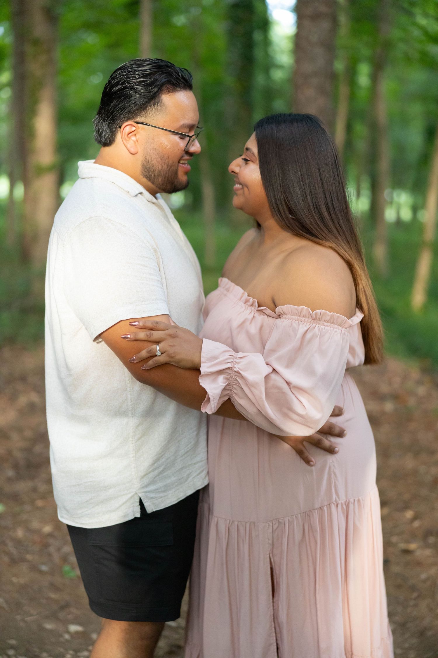 A couple in white and pink outfits share romantic moments together in a wooded outdoor setting.