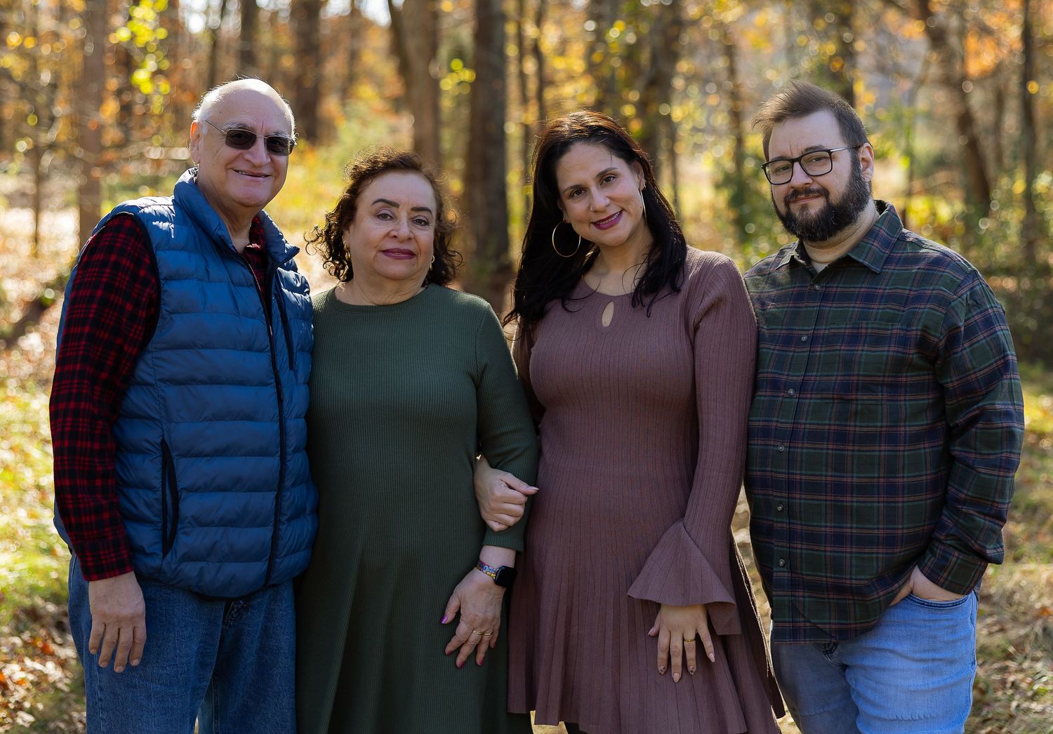 A group of people pose together outdoors on a sunny autumn day with golden fall foliage in the background.