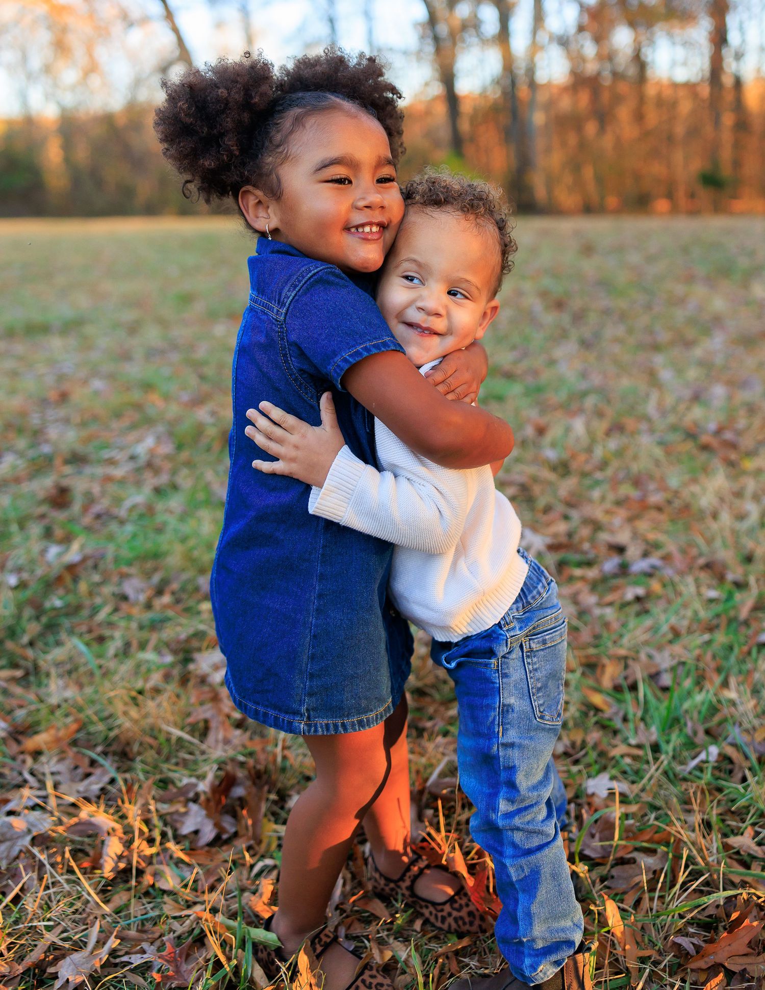 Two children hug and laugh while playing in fallen autumn leaves.
