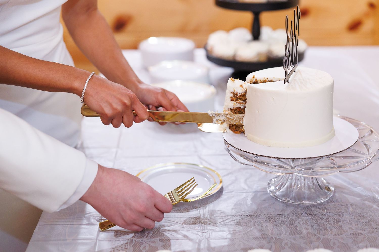 Hands using cake decorating tools to frost and smooth the sides of a white layer cake on a cake stand.