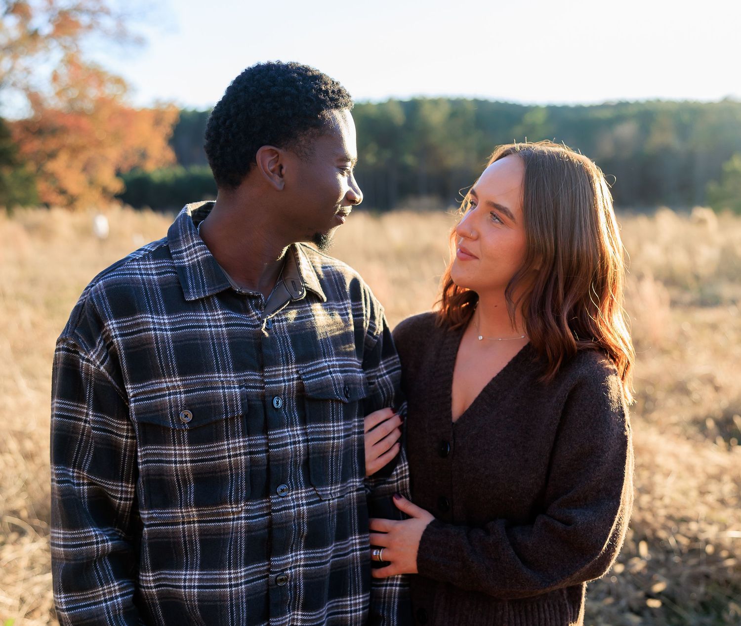 A couple shares intimate moments in a golden field during sunset while wearing plaid and black outfits.